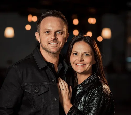 A smiling man and woman posing together indoors with warm lighting.