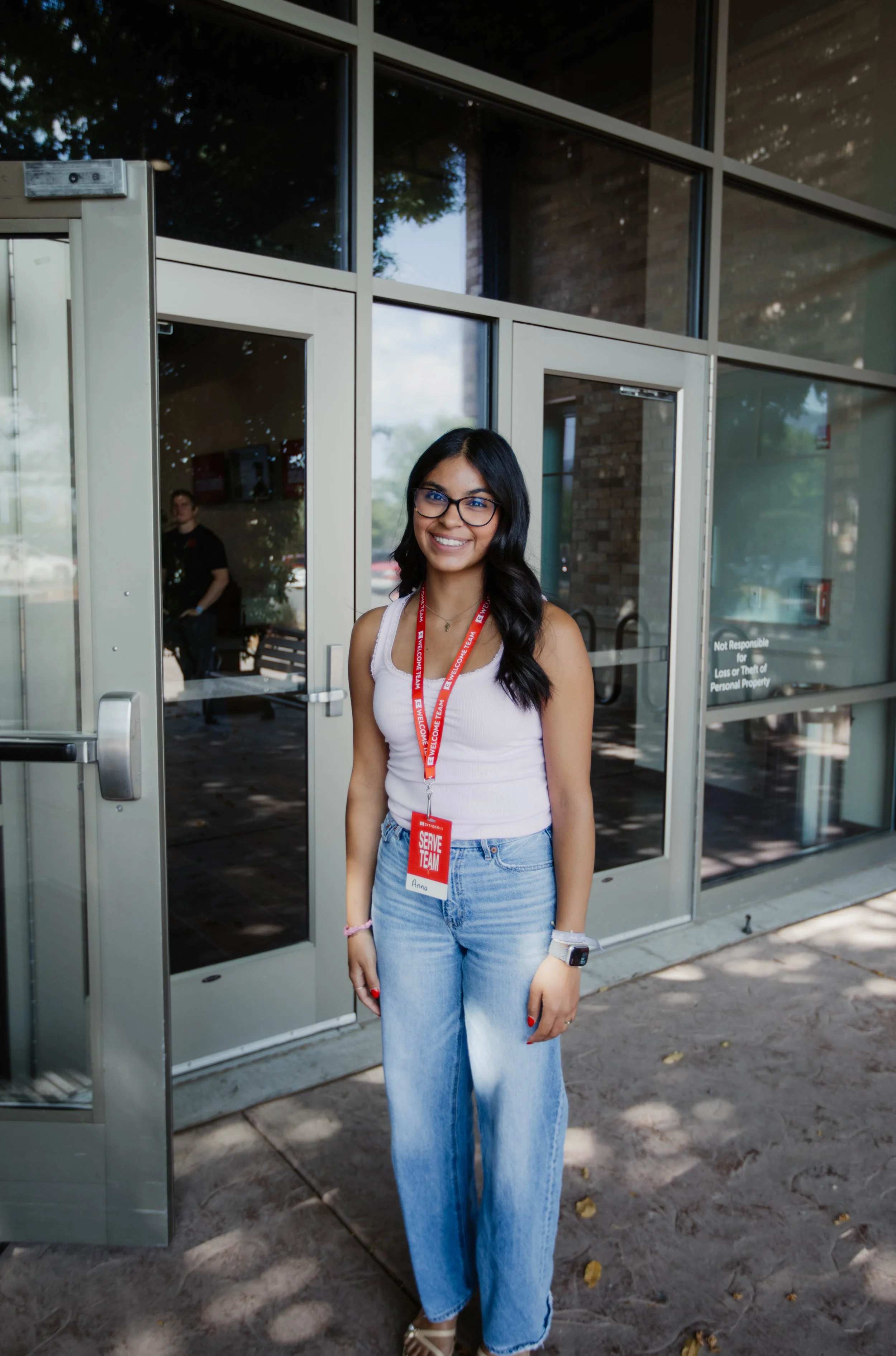 Group of six young adults smiling at the camera indoors, holding cups and snacks, with a mural of a person's face on the wall behind them.