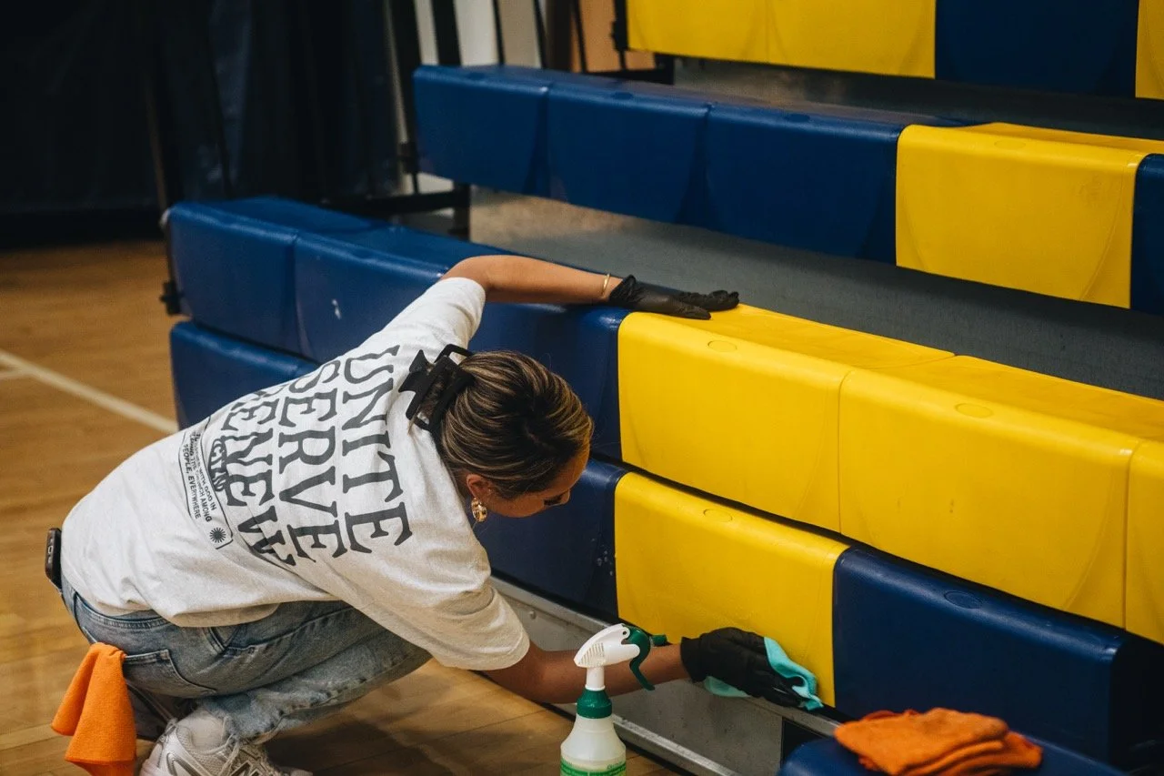 A person cleaning yellow and blue stadium seats in an indoor gymnasium.