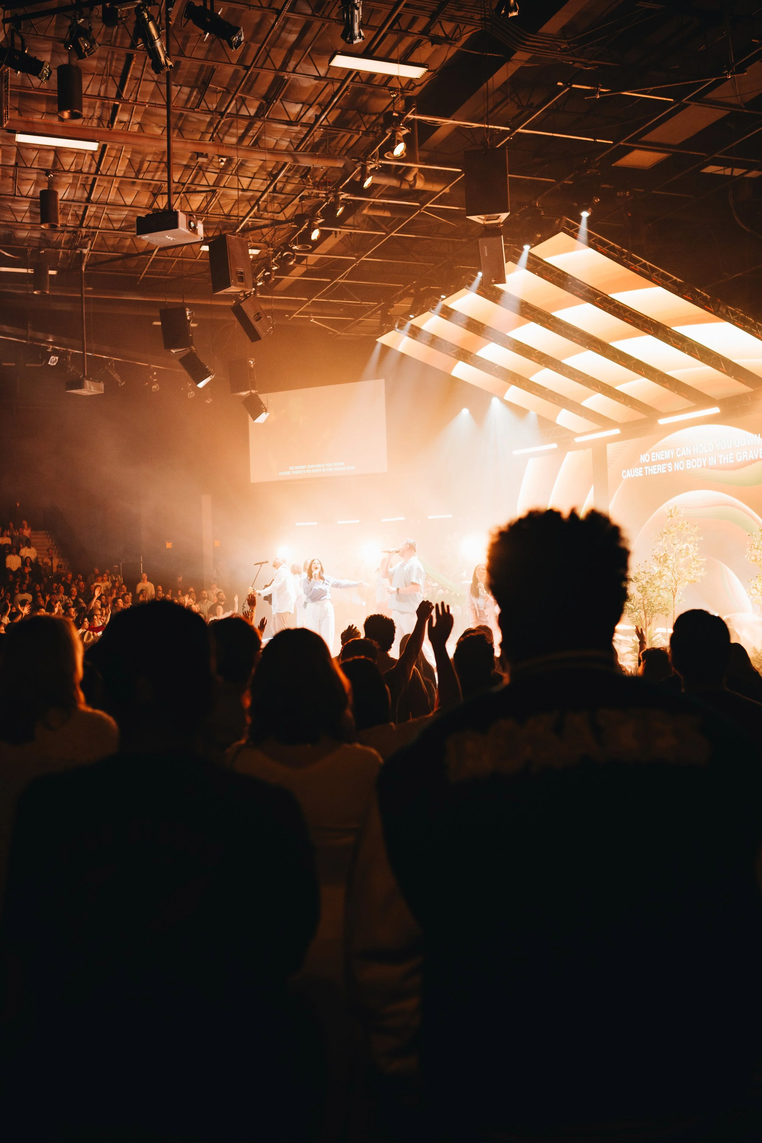 People attending a concert or musical performance in a large indoor venue with stage lighting and performers on stage.