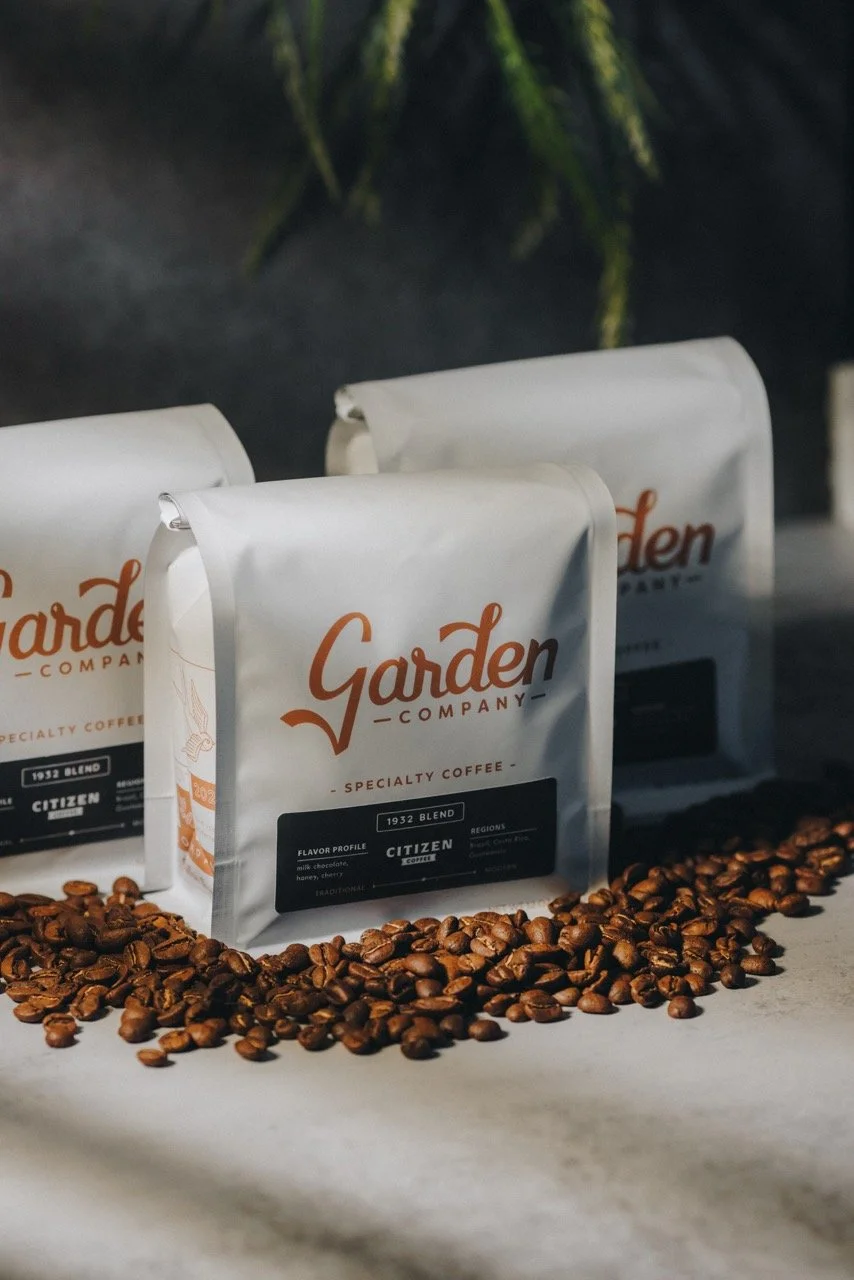 Coffee bags labeled Garden Company Specialty Coffee with coffee beans spilled in front.
