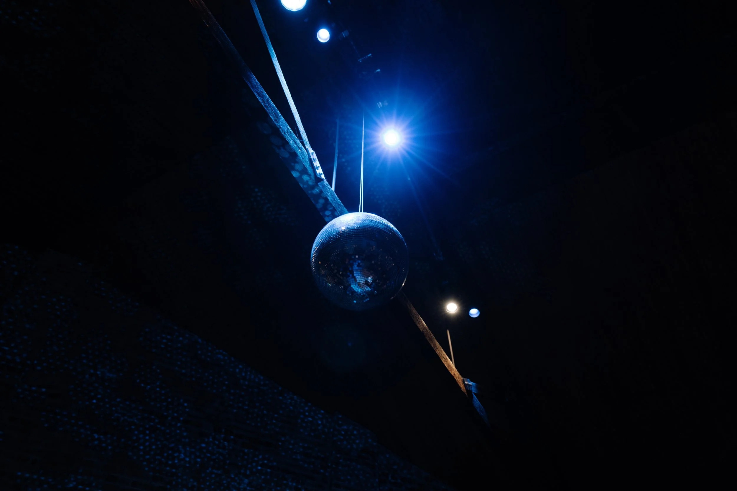 A disco ball hanging from the ceiling, illuminated by bright blue lights in a dark room.