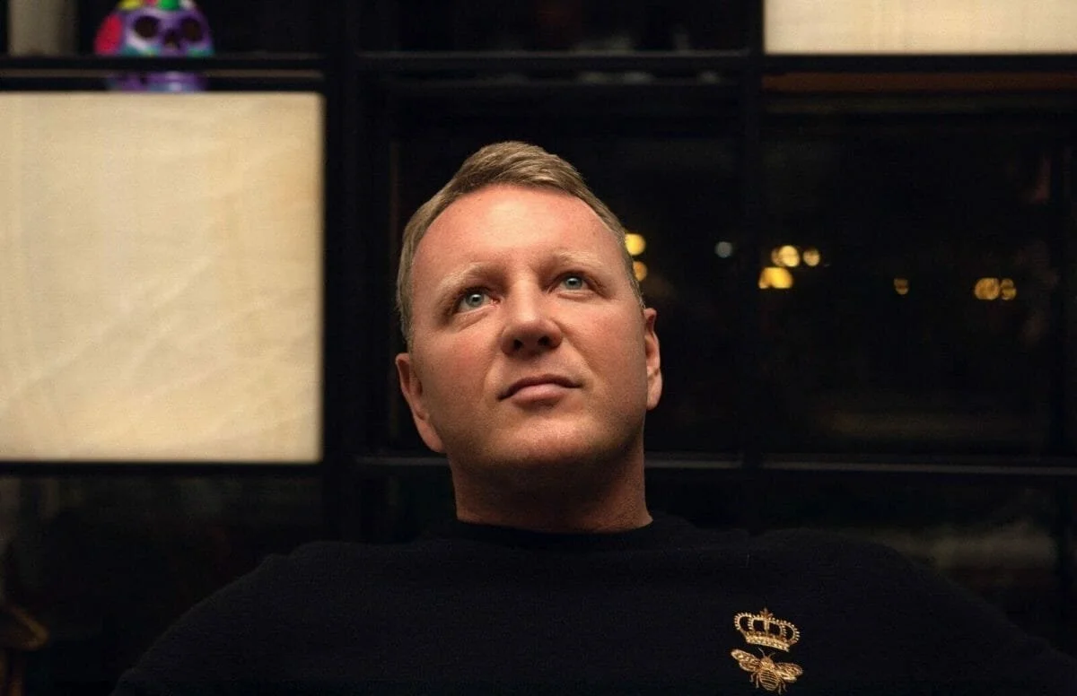Polished portrait of Chad Willis in a black sweater with a gold emblem, heavily edited to smooth skin and reshape features, inconsistent with his natural appearance.