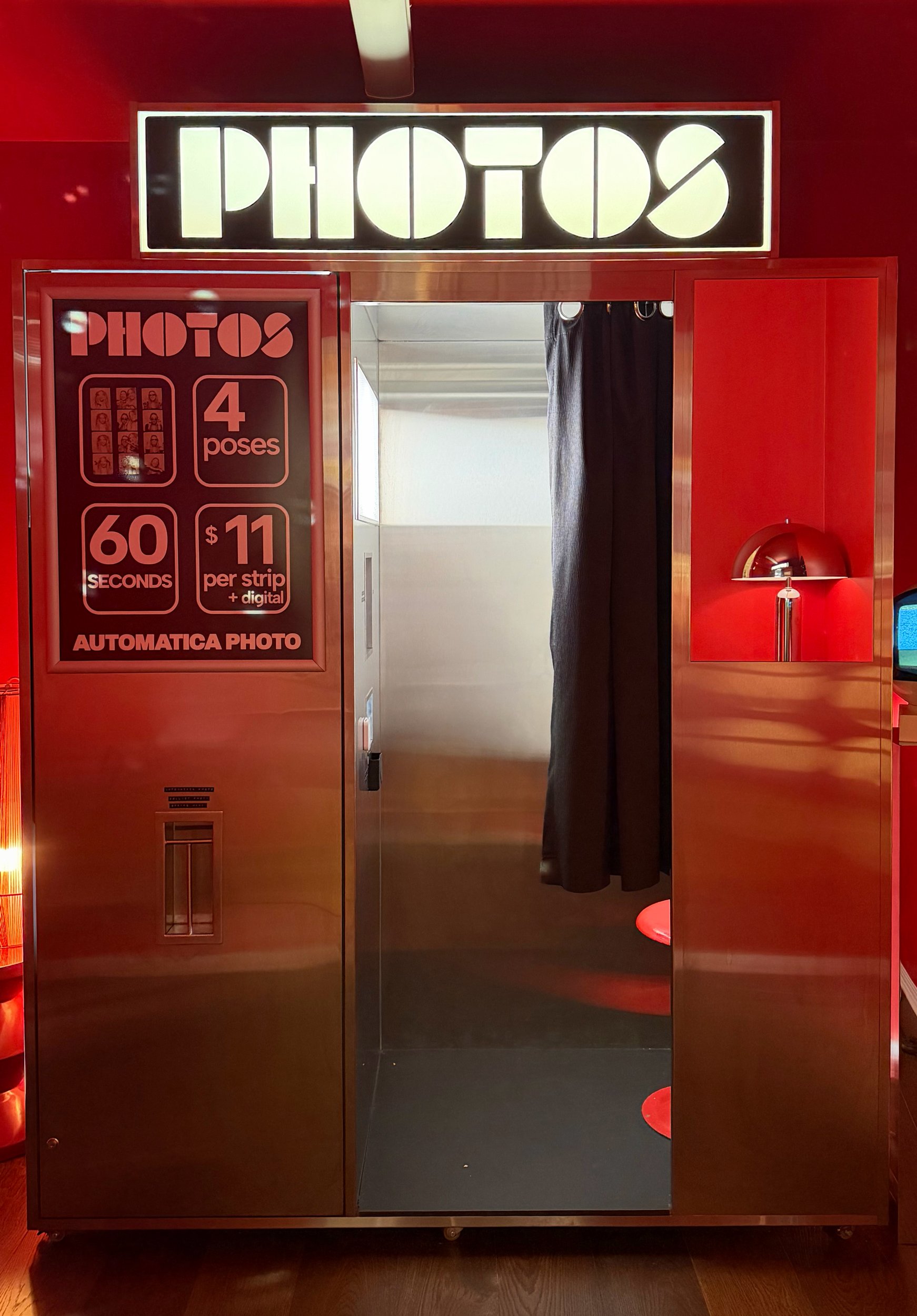 Chrome photo booth at Automatica Photo in Burleigh Heads, with an illuminated PHOTOS sign, black curtain and warm red lighting.