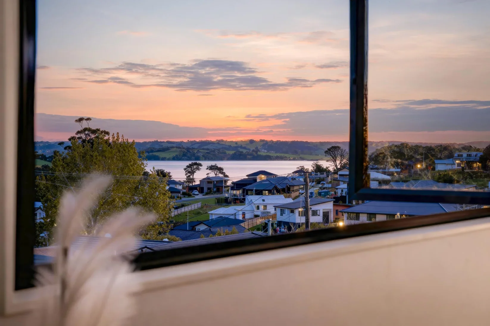 View of a Snells Beach neighborhood and lake at sunset seen through a window.