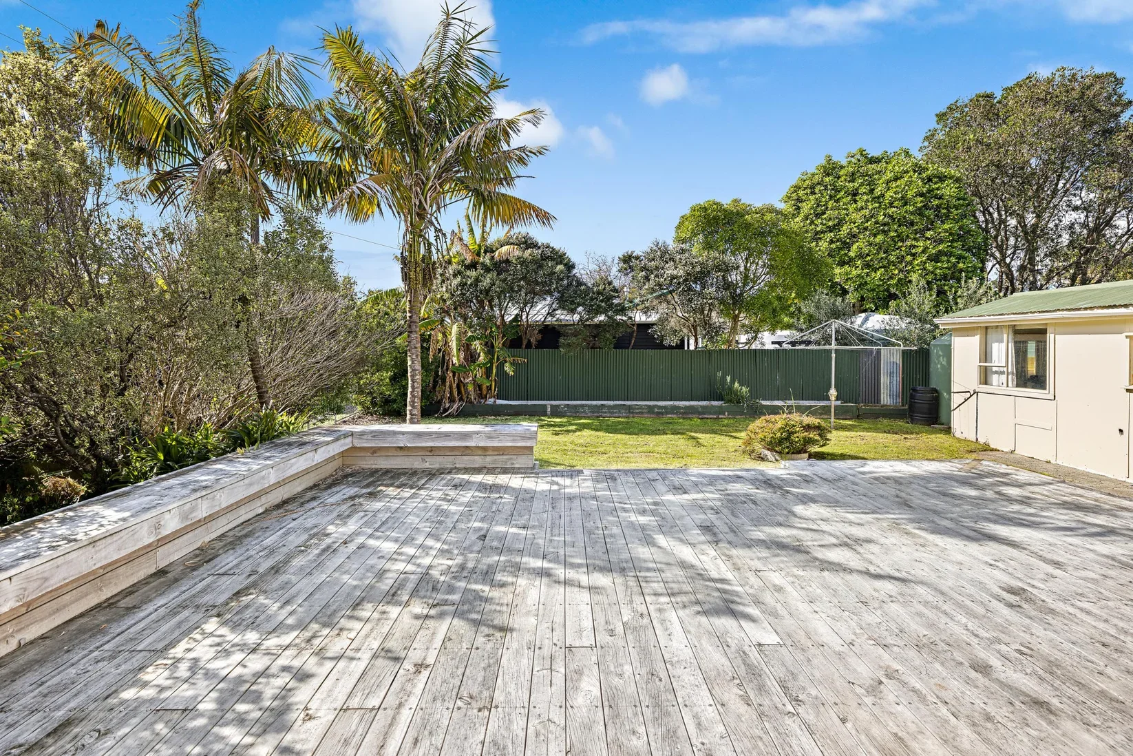 Outdoor backyard with wooden deck, green grass, trees, and a beige house with a green roof.