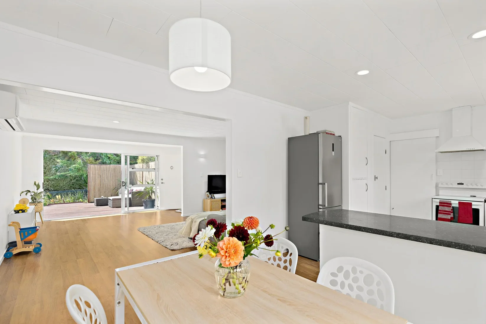 Open plan living and dining area with sliding glass doors leading to a backyard patio, a kitchen with a gray refrigerator, and a dining table with a floral centerpiece.