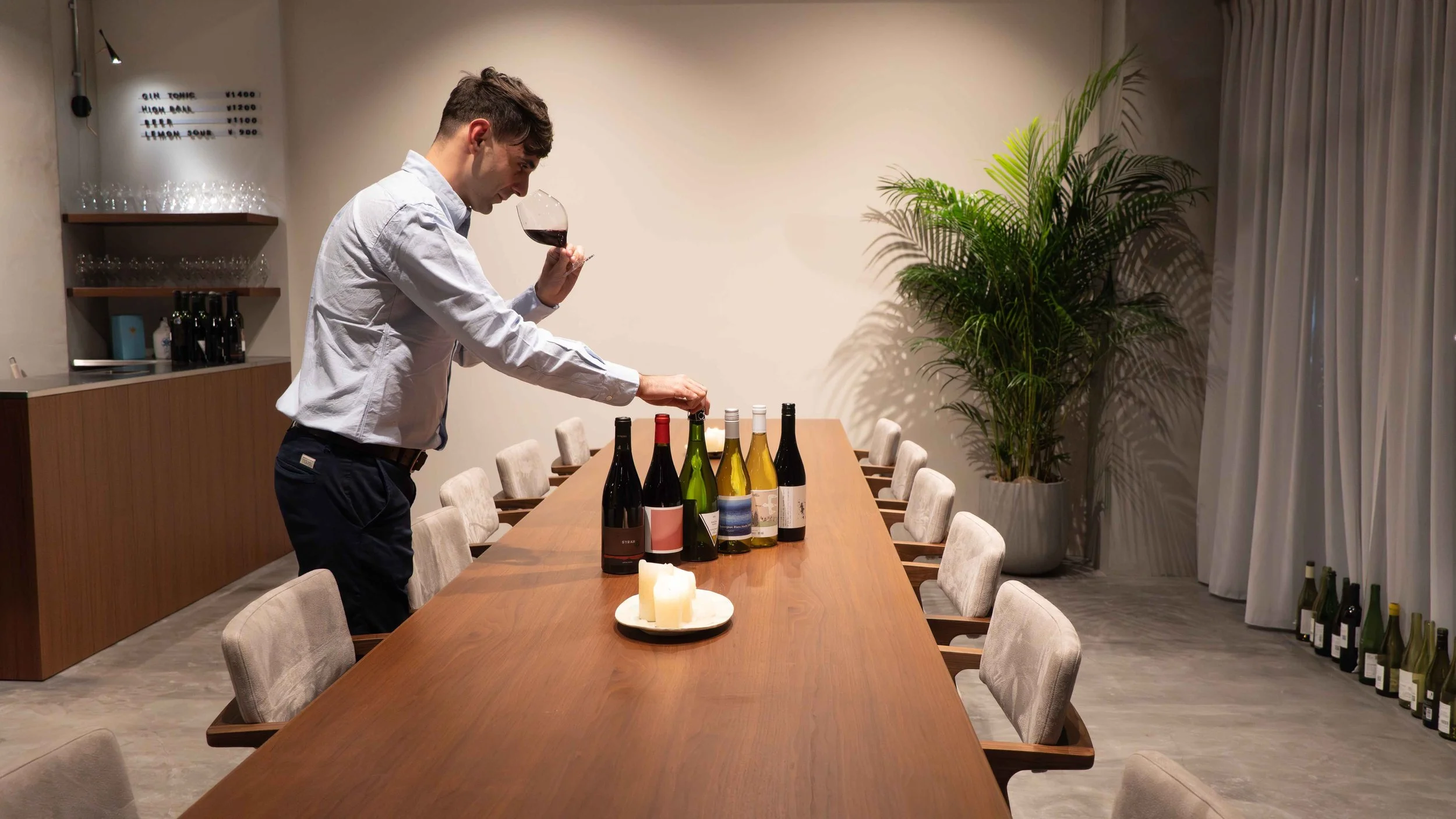 Wine expert evaluating Japanese wine at the THREE GRAPES daytime wine bar, with curated bottles.