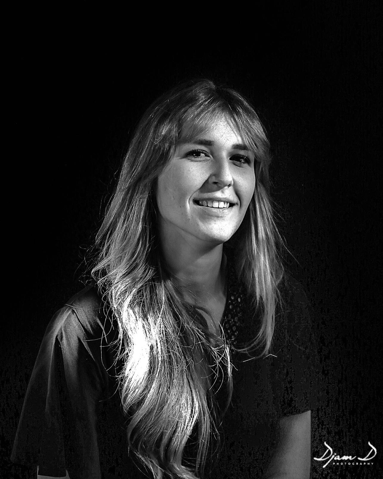 Portrait en noir et blanc d'une jeune femme avec de longs cheveux ondulés et un sourire.