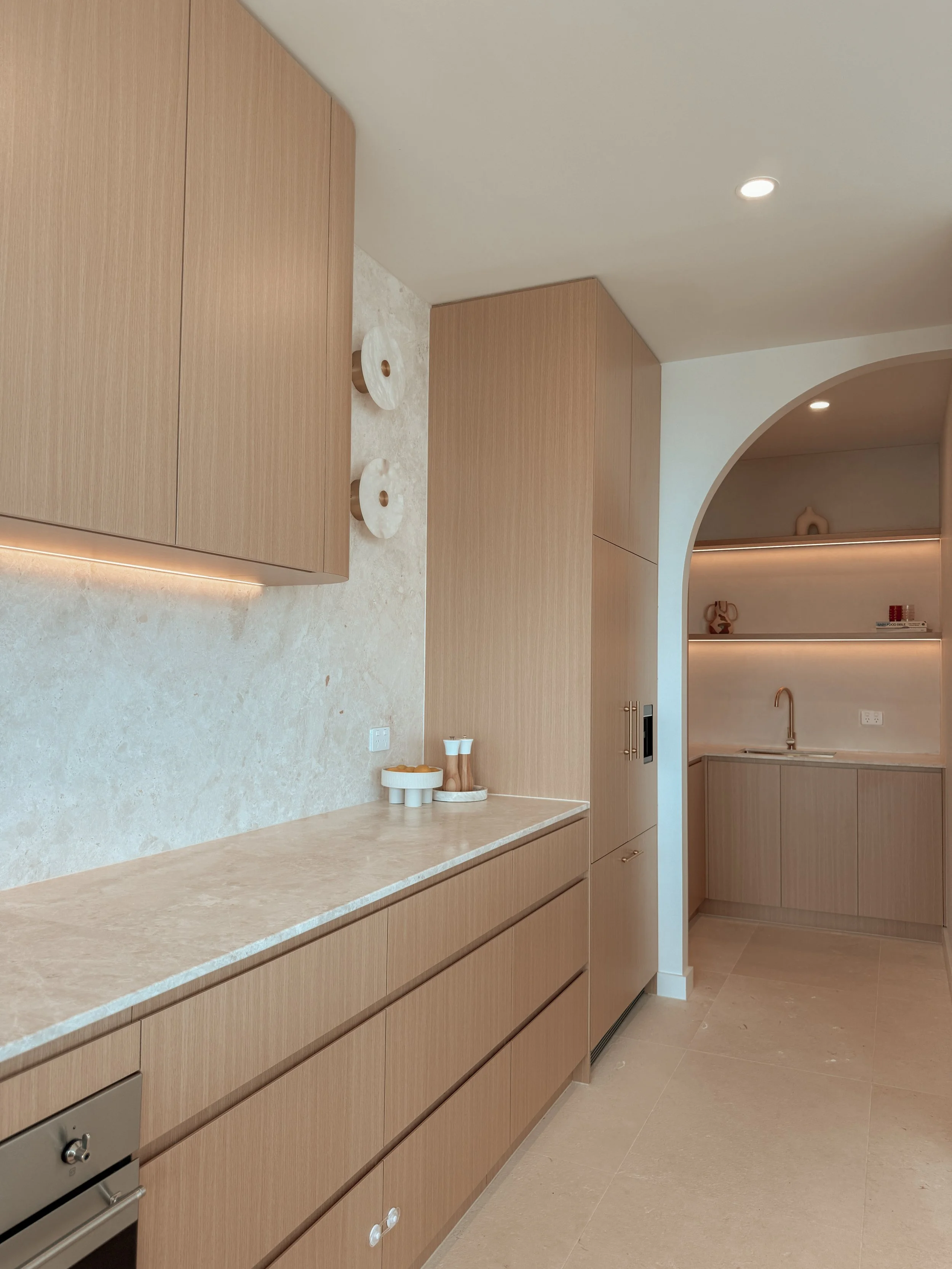 Pantry behind a curved archway featuring open shelving, brass tapware, and vertical white tiles