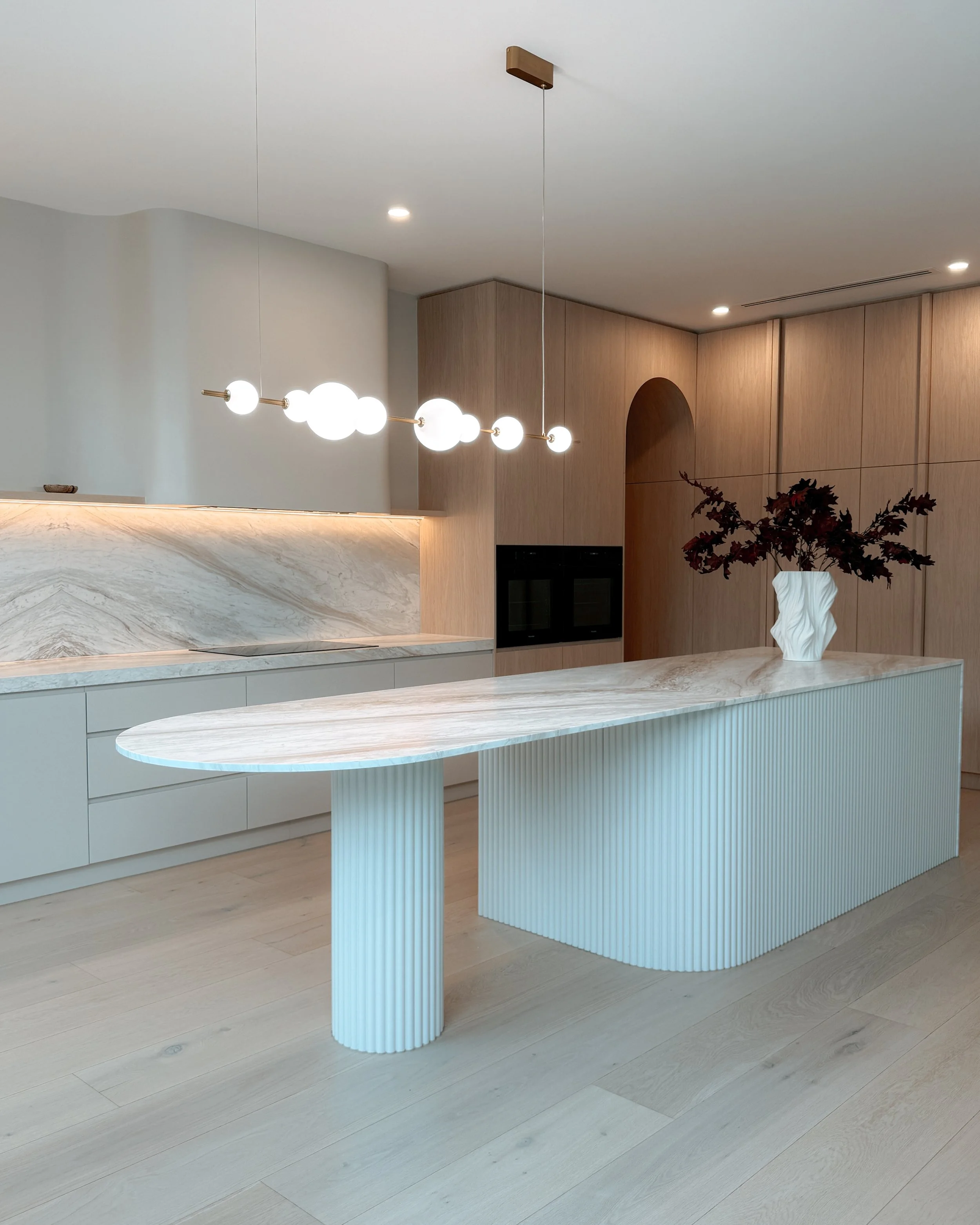 Contemporary soft-curved kitchen with fluted island, light timber cabinetry, and sculptural rangehood in a minimal-luxe Melbourne new-build. Designed by TID Studio, interior design in Sydney