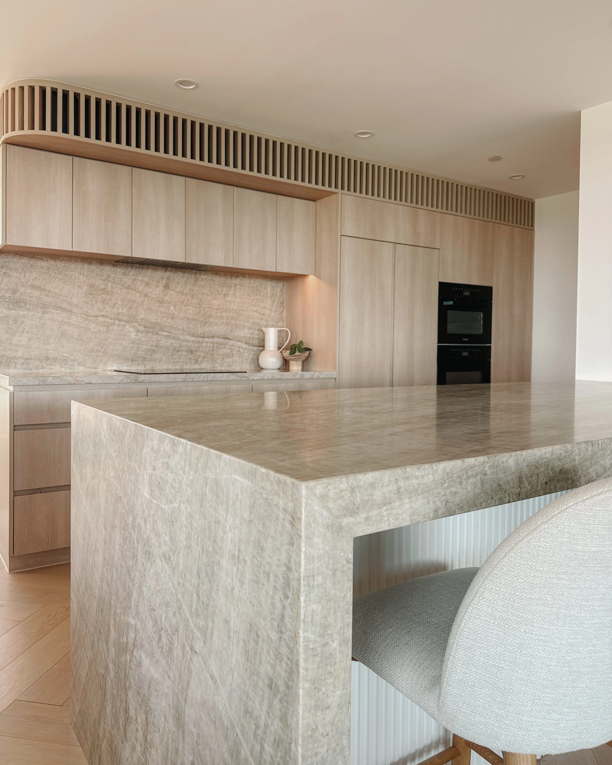 Contemporary condo renovation, modern coastal kitchen with curved island in Taj Mahal stone and pale timber cabinetry in Oceanview Apartment in Gold Coast. Designed by TID Studio Sydney