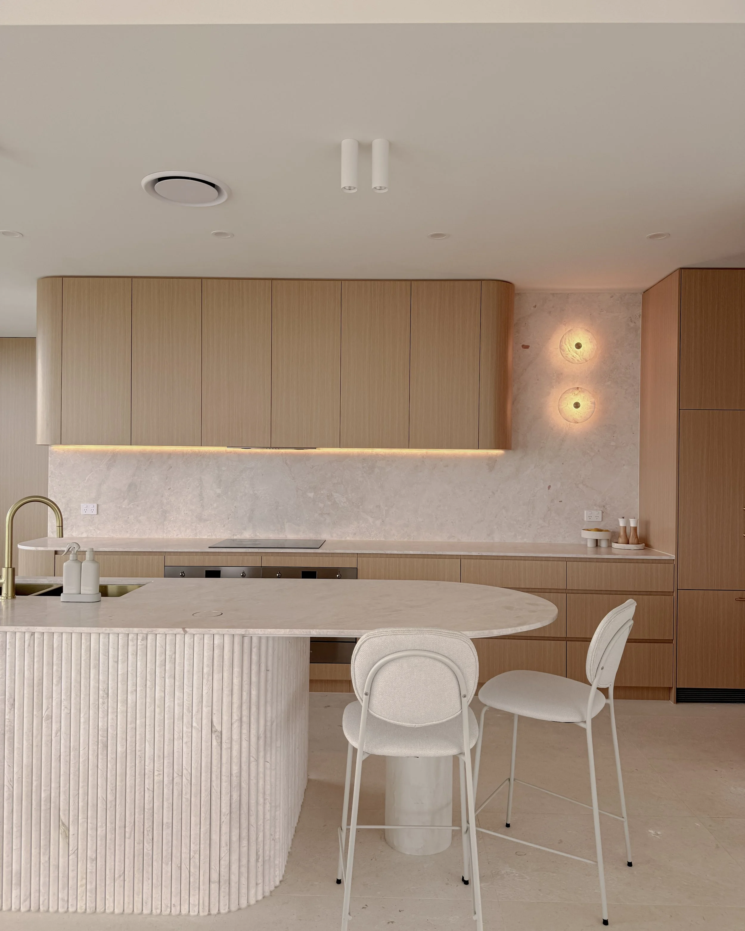 Modern coastal kitchen and pantry designed by TID Studio. Contemporary kitchen with curved cabinetry and fluted stone kitchen island. Sydney interior designer