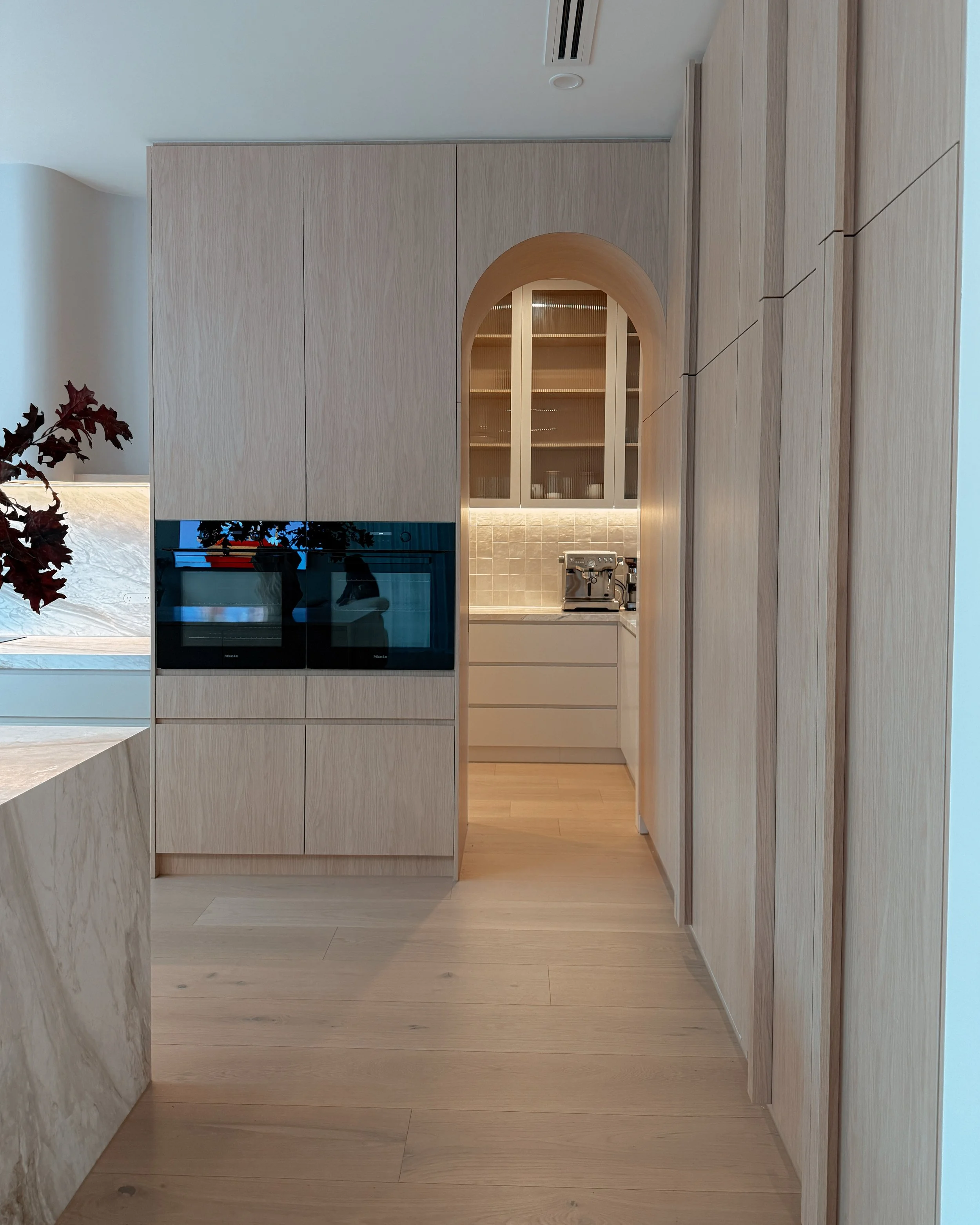 Contemporary soft-curved kitchen with fluted island, light timber cabinetry, and sculptural rangehood in a minimal-luxe Melbourne new-build. Designed by TID Studio, interior design in Sydney
