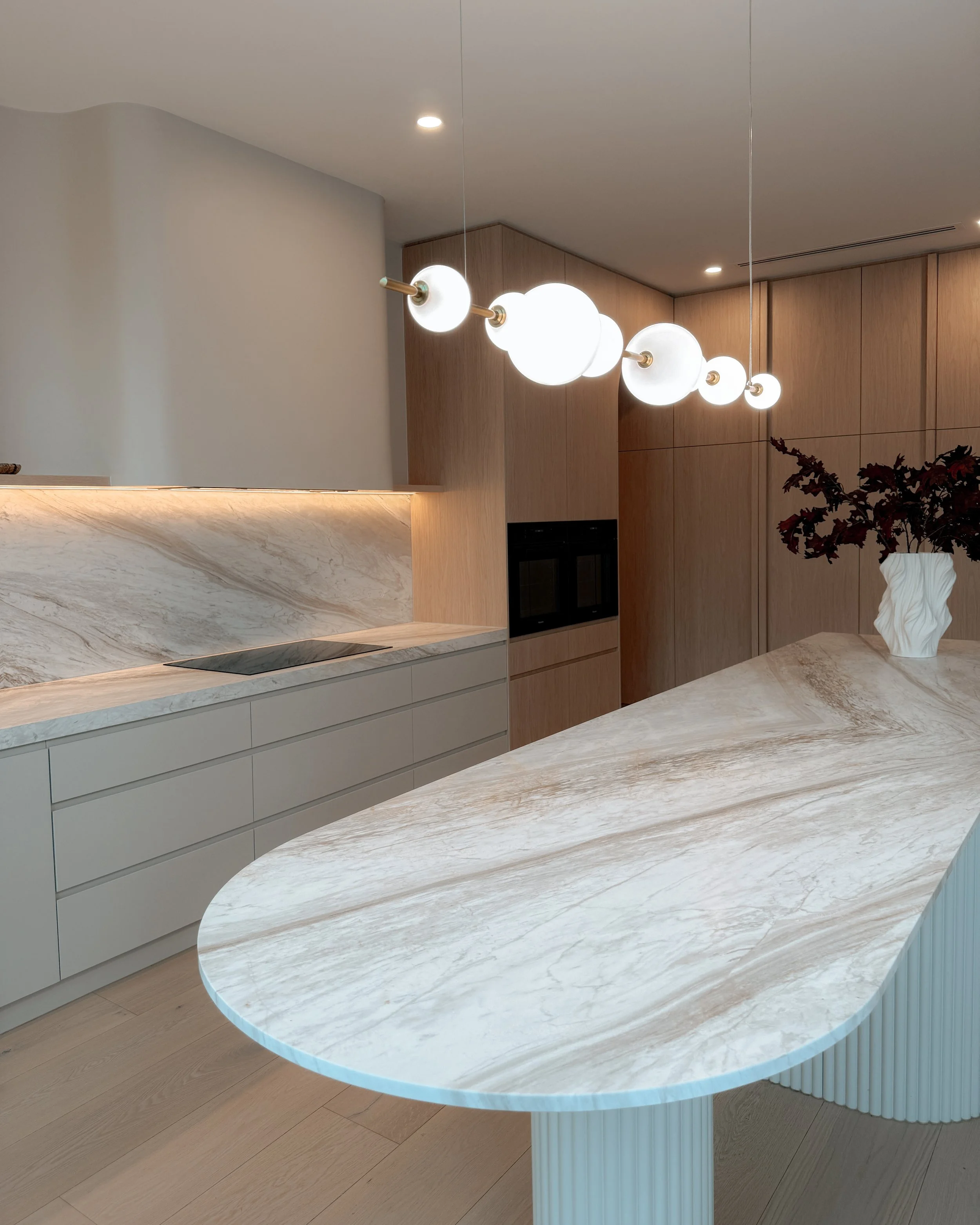Contemporary soft-curved kitchen with fluted island, light timber cabinetry, and sculptural rangehood in a minimal-luxe Melbourne new-build. Designed by TID Studio, interior design in Sydney