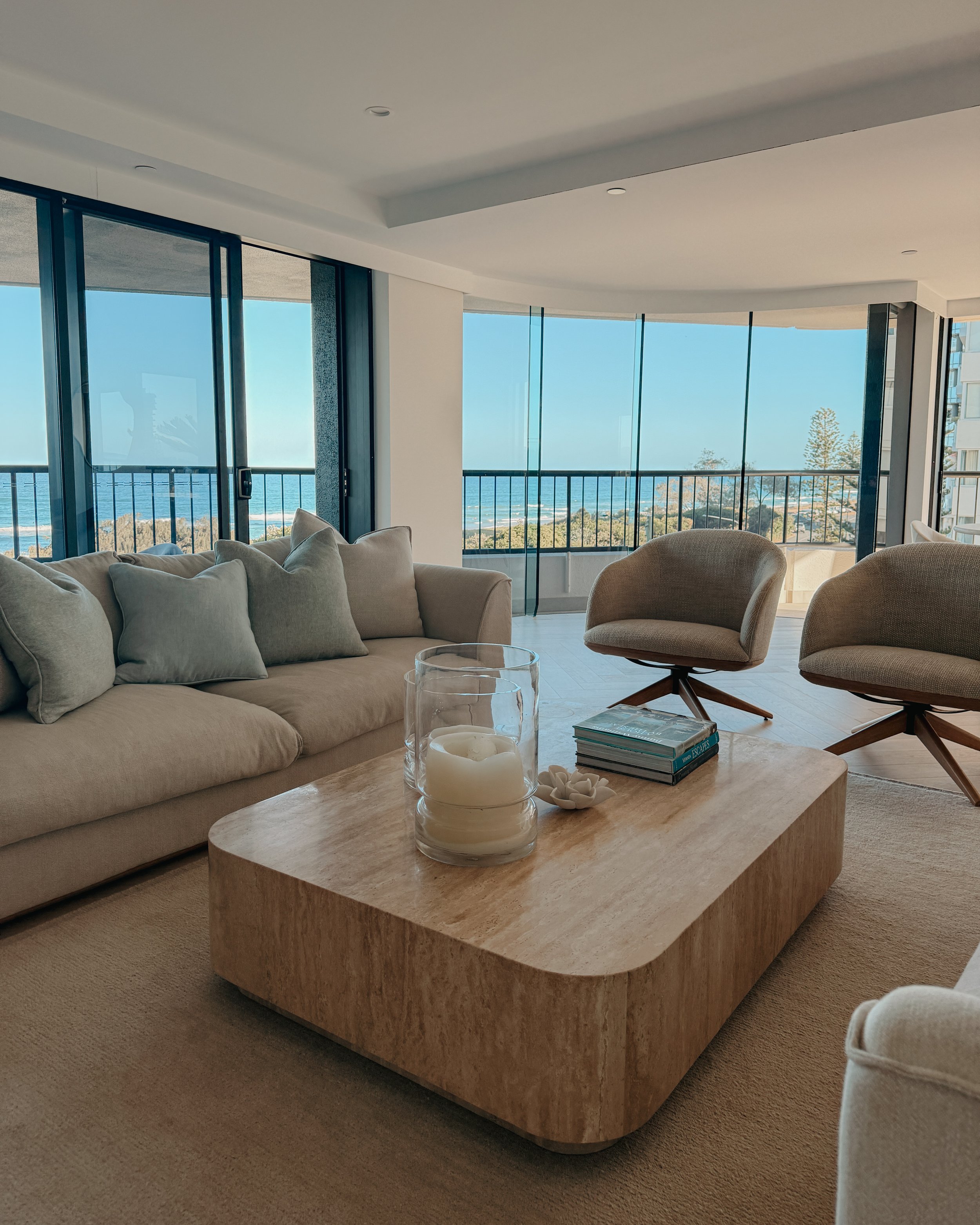 Contemporary condo renovation, modern coastal kitchen with curved island in Taj Mahal stone and pale timber cabinetry, living room seating area in Oceanview Apartment in Gold Coast. Designed by TID Studio Sydney