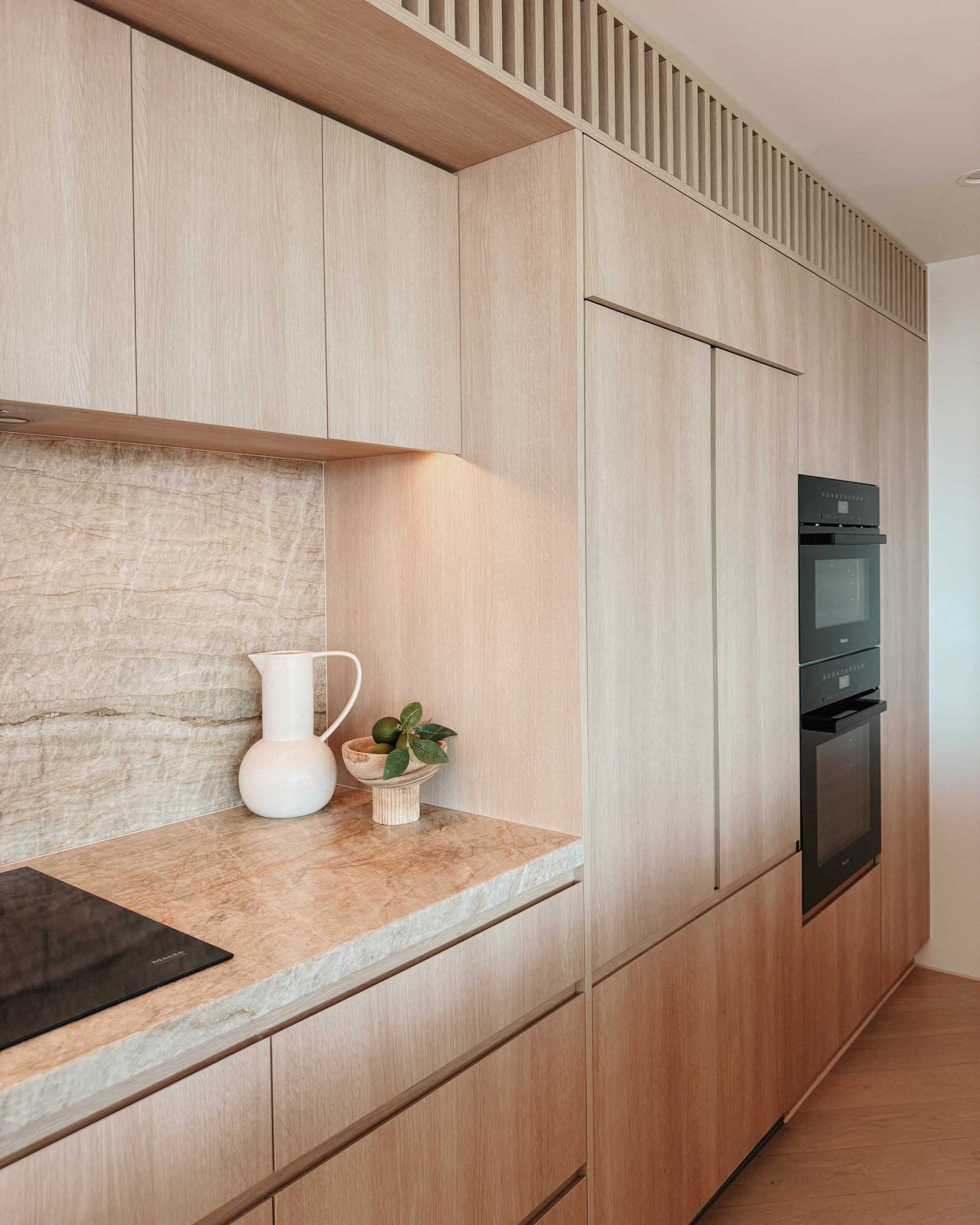 Contemporary condo renovation, modern coastal kitchen with curved island in Taj Mahal stone and pale timber cabinetry in Oceanview Apartment in Gold Coast. Designed by TID Studio Sydney