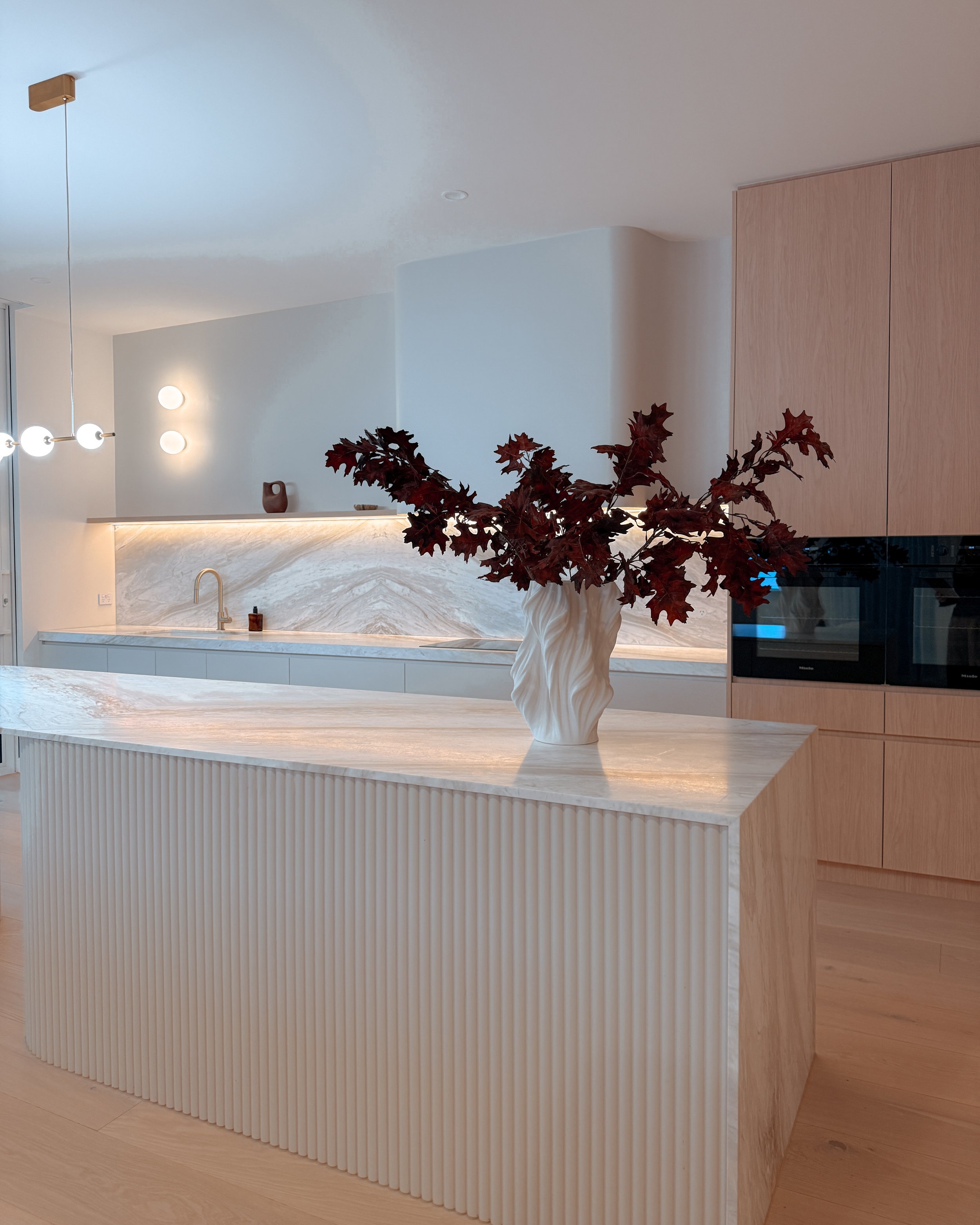 Contemporary soft-curved kitchen with fluted island, light timber cabinetry, and sculptural rangehood in a minimal-luxe Melbourne new-build. Designed by TID Studio, interior design in Sydney