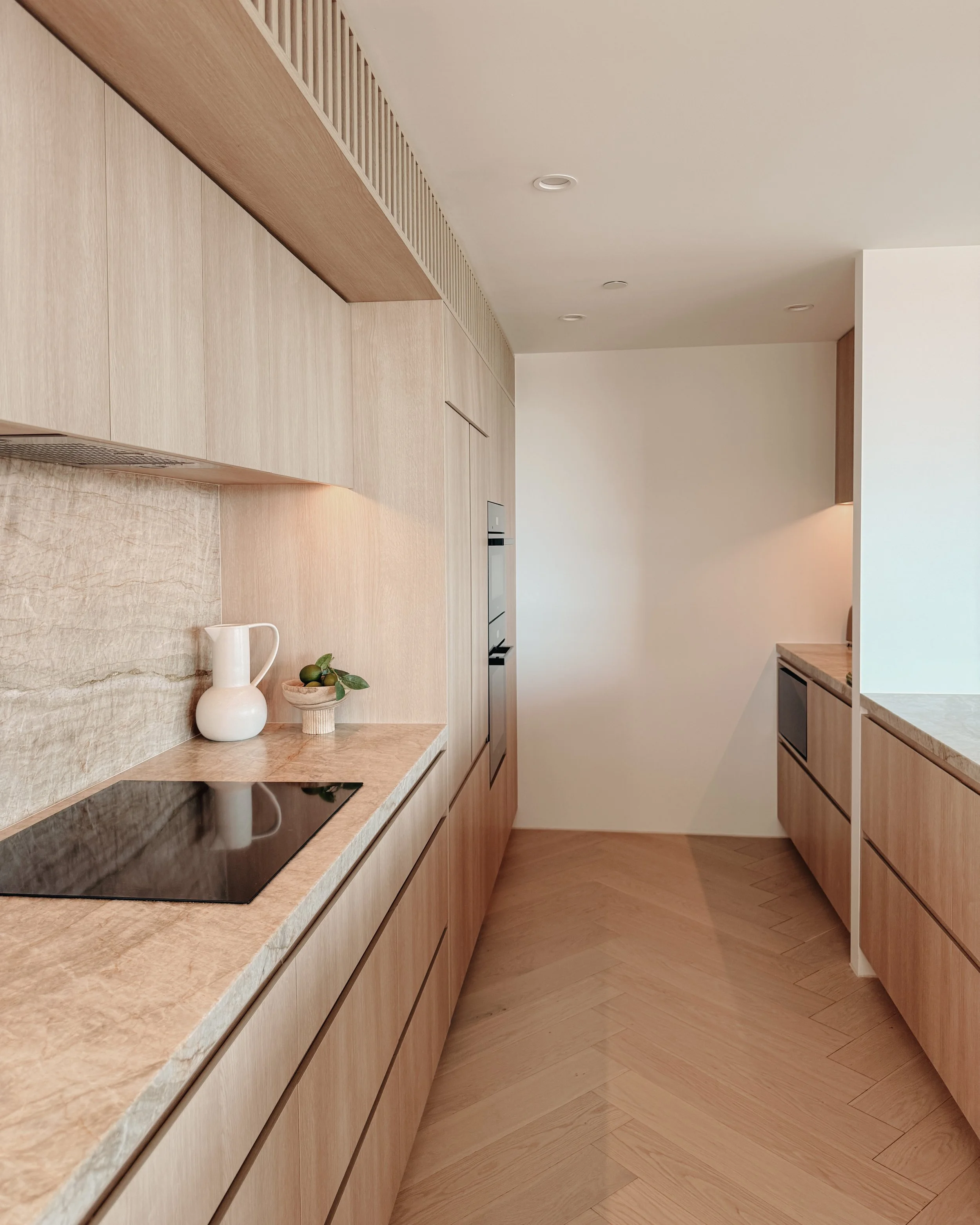 Contemporary condo renovation, modern coastal kitchen with curved island in Taj Mahal stone and pale timber cabinetry in Oceanview Apartment in Gold Coast. Designed by TID Studio Sydney