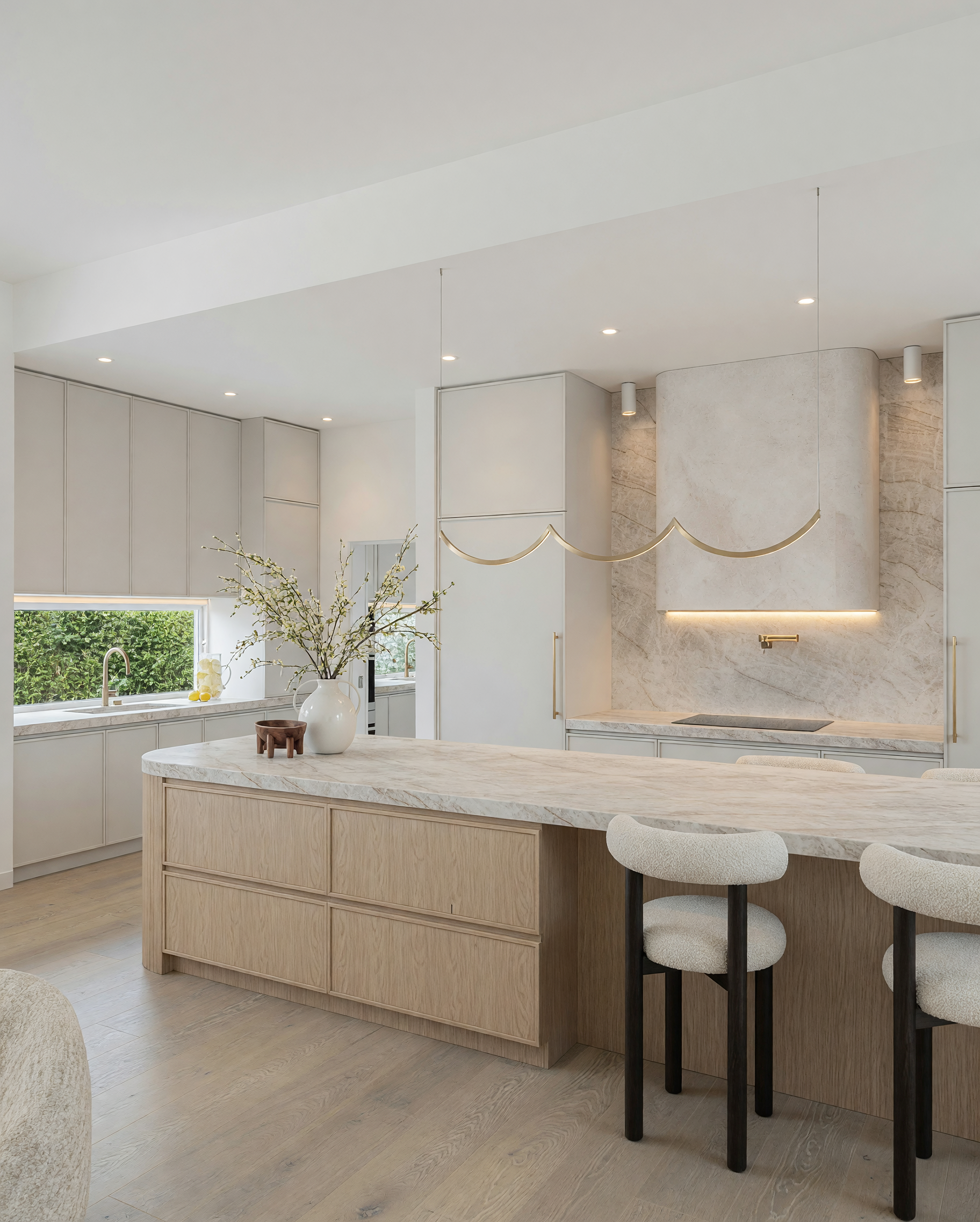 Modern luxury kitchen featuring Taj Mahal stone curved island, warm oak cabinetry, bronze rangehood and custom pantry design