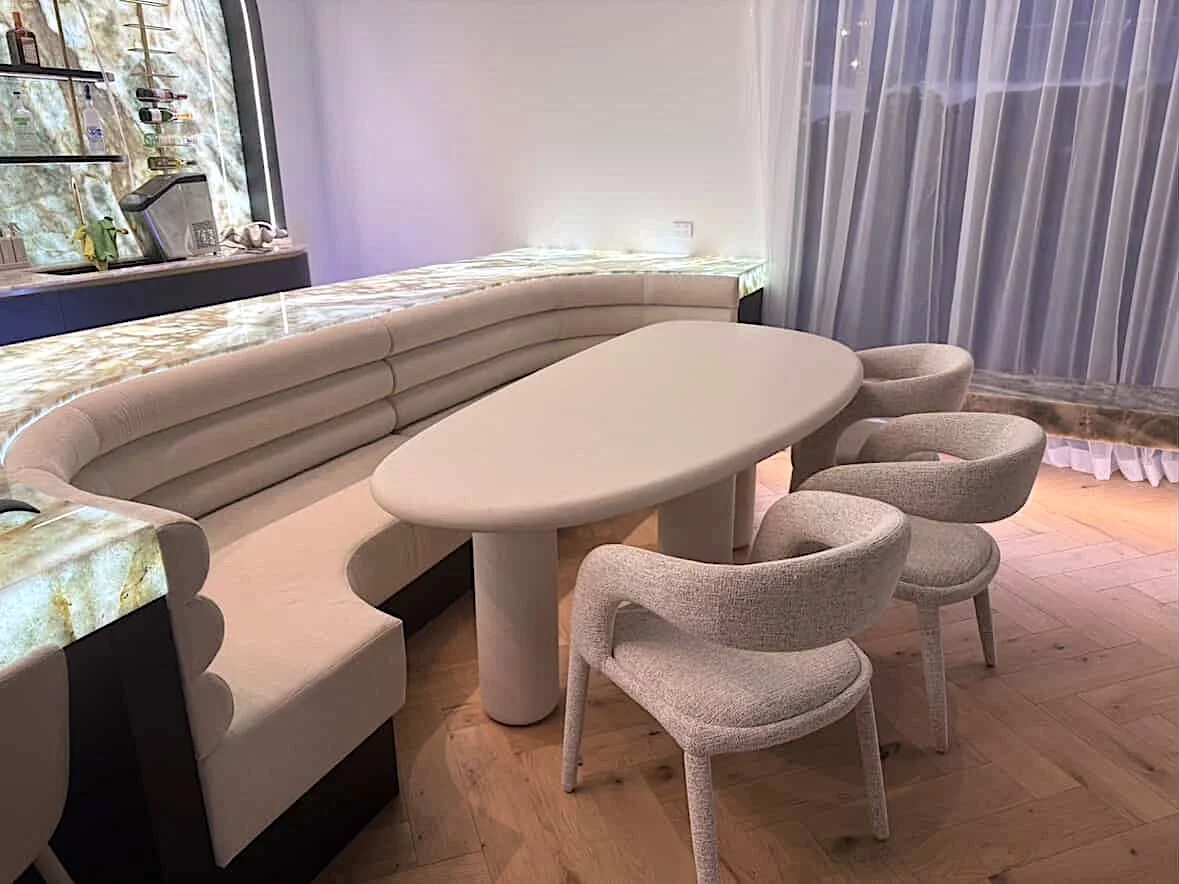 Soft neutral pool house with custom curved backlit bar and island with integrated banquette, modular sofa with fireplace anchored by stone benchseat on the sides, and warm minimal styling designed by TID Studio in Sydney