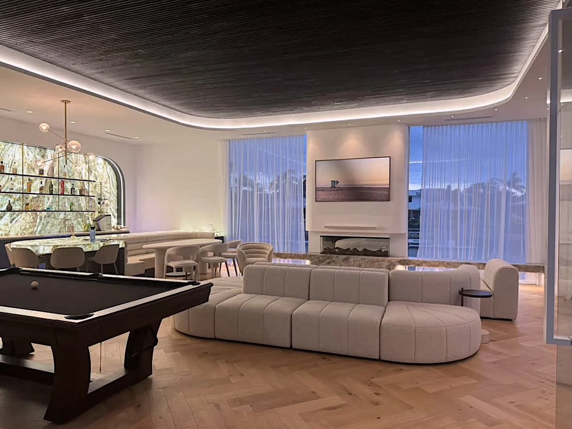 Soft neutral pool house with custom curved backlit bar and island with integrated banquette, modular sofa with fireplace anchored by stone benchseat on the sides, and warm minimal styling designed by TID Studio in Sydney