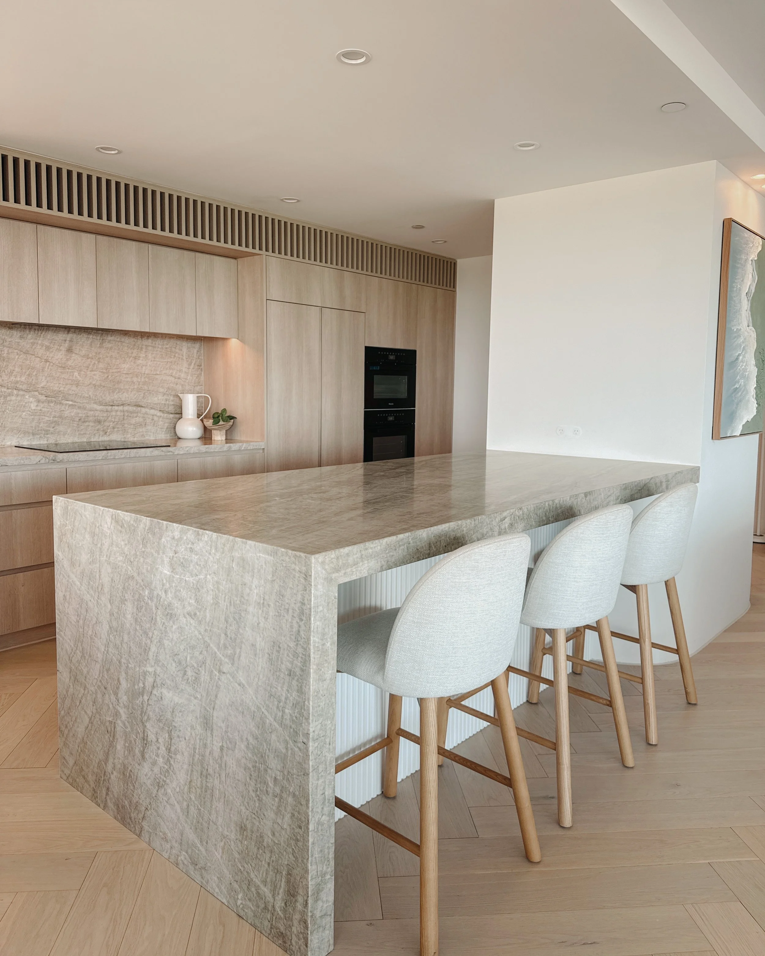 Modern kitchen with Taj  Mahal stone, curved island, and warm timber tones — coastal apartment design by TID Studio Gold Coast