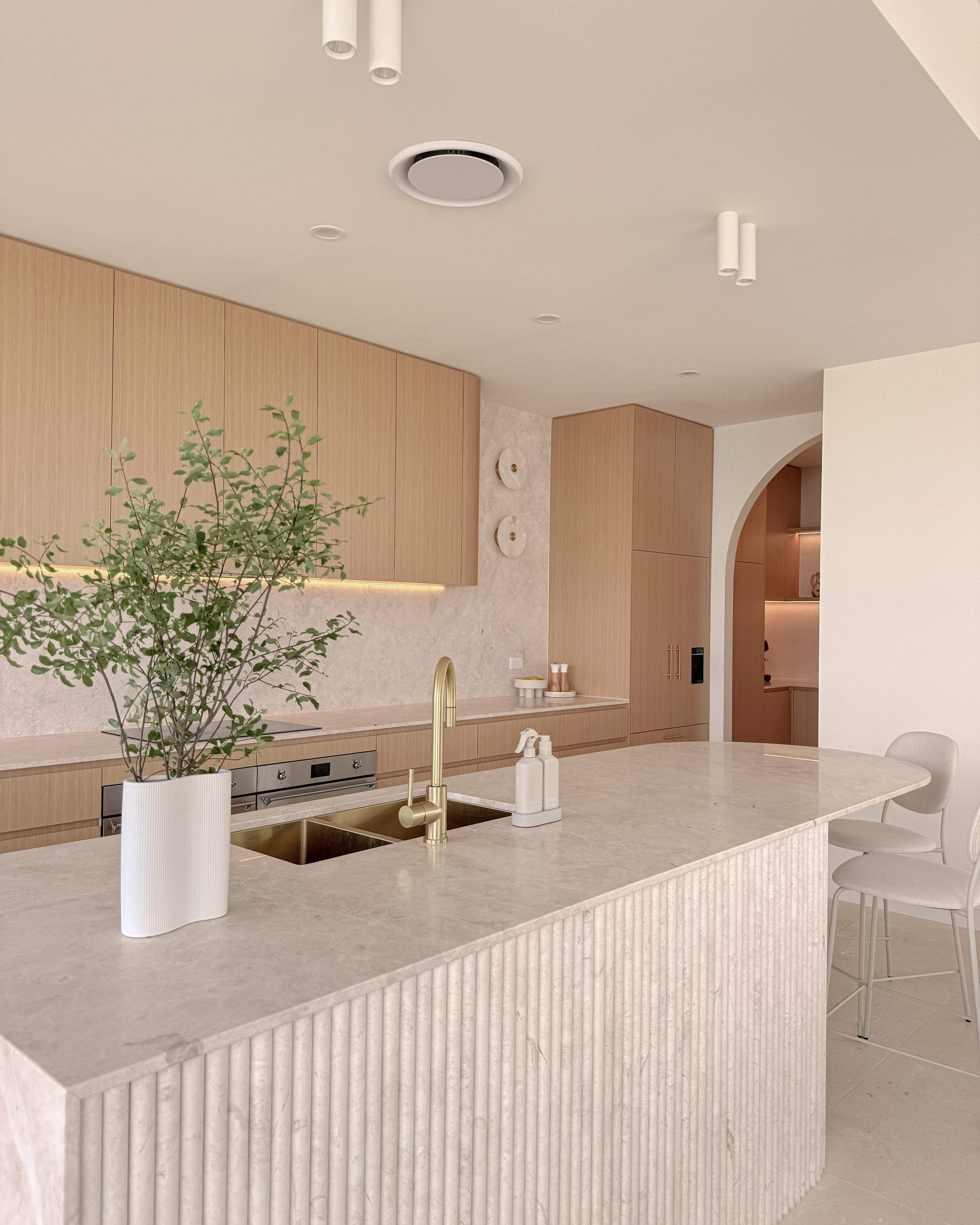 Modern coastal kitchen and pantry designed by TID Studio. Contemporary kitchen with curved cabinetry and fluted stone kitchen island. Sydney interior designer