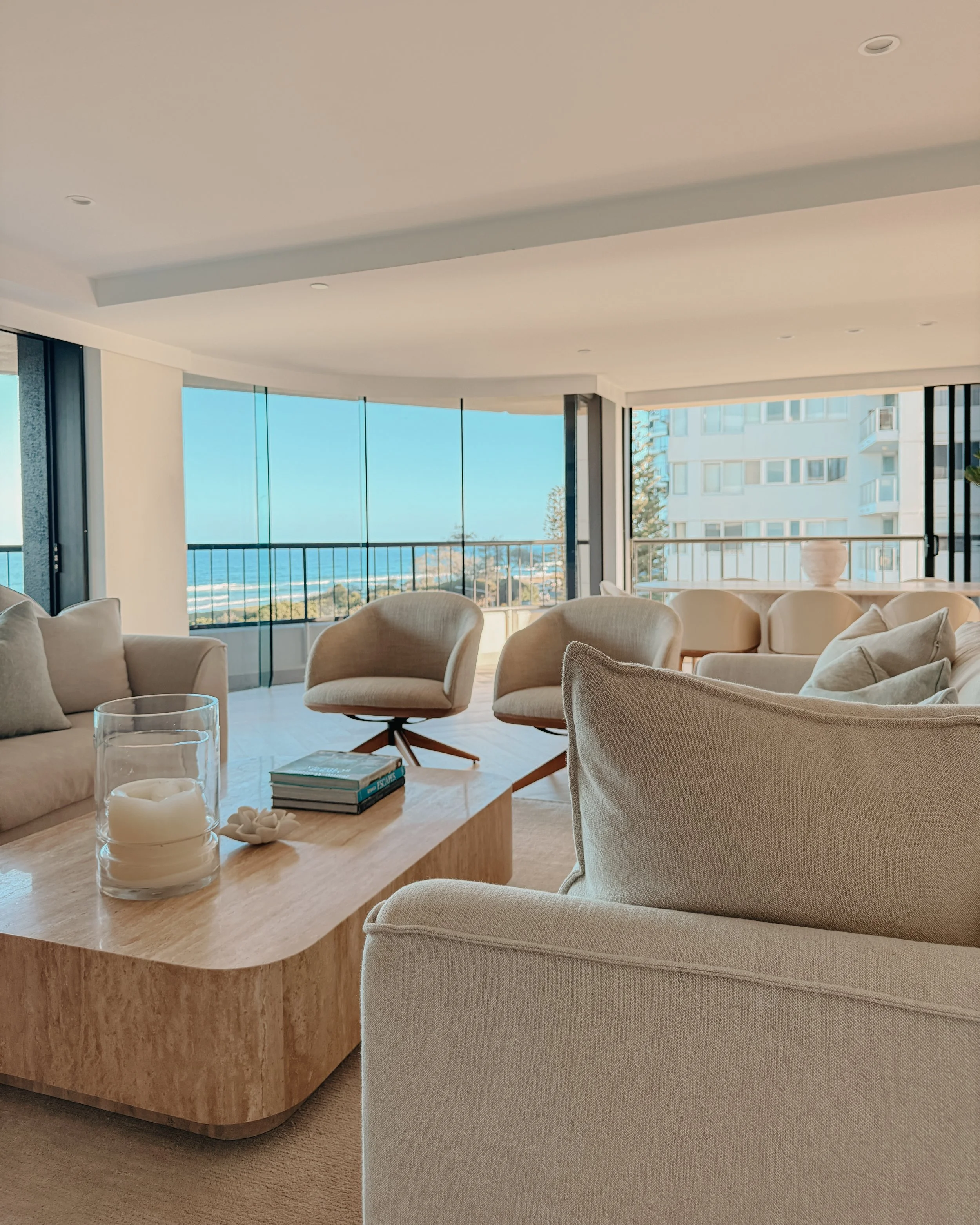 Contemporary condo renovation, modern coastal kitchen with curved island in Taj Mahal stone and pale timber cabinetry, living room seating area in Oceanview Apartment in Gold Coast. Designed by TID Studio Sydney