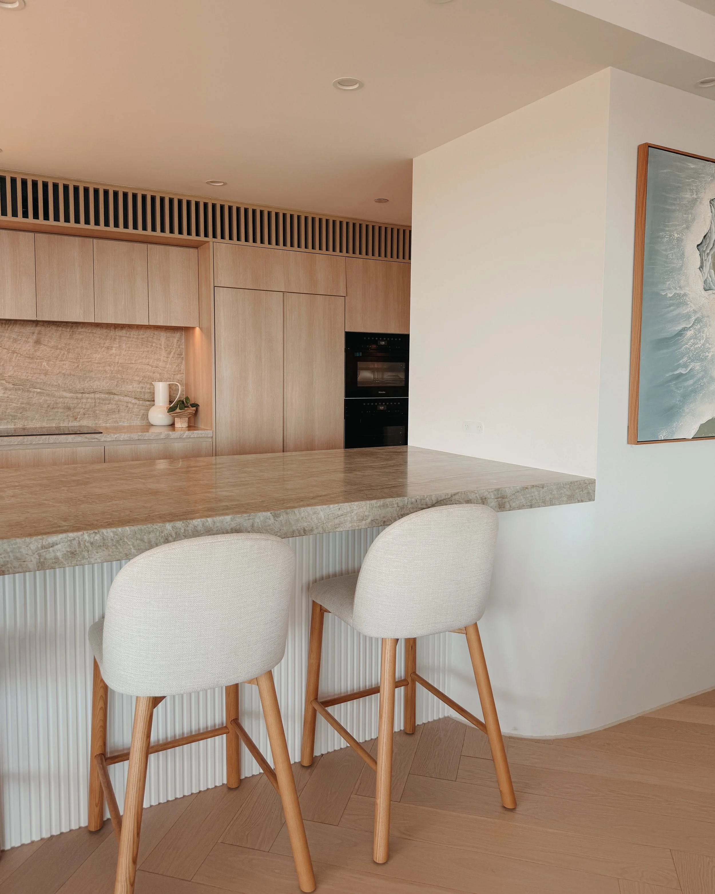 Contemporary condo renovation, modern coastal kitchen with curved island in Taj Mahal stone and pale timber cabinetry in Oceanview Apartment in Gold Coast. Designed by TID Studio Sydney