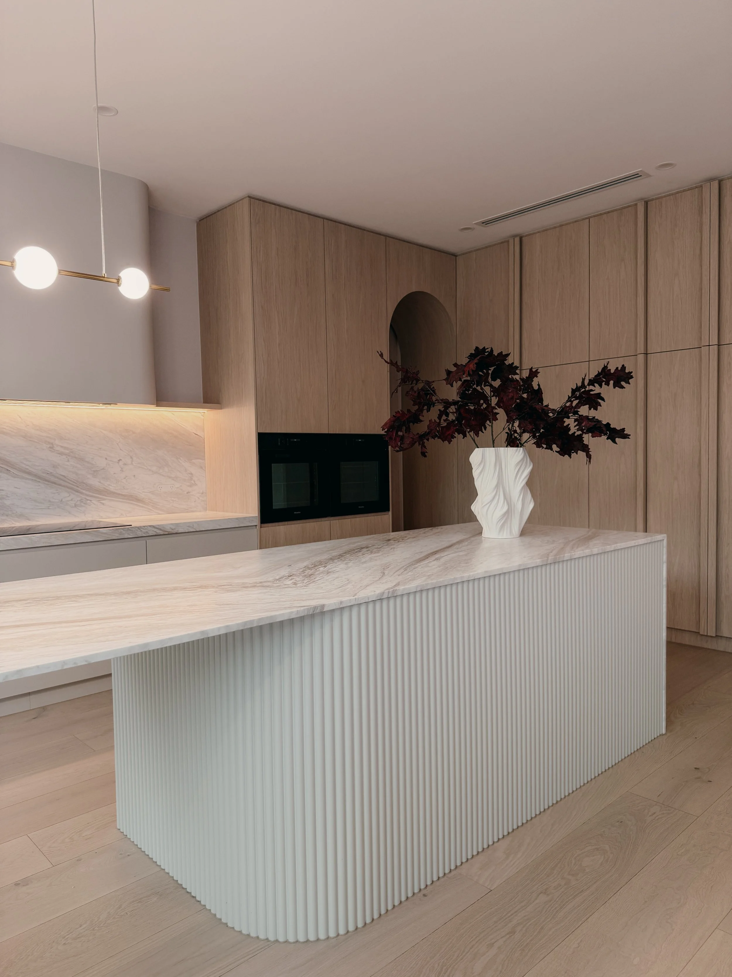 Contemporary soft-curved kitchen with fluted island, light timber cabinetry, and sculptural rangehood in a minimal-luxe Melbourne new-build. Designed by TID Studio, interior design in Sydney