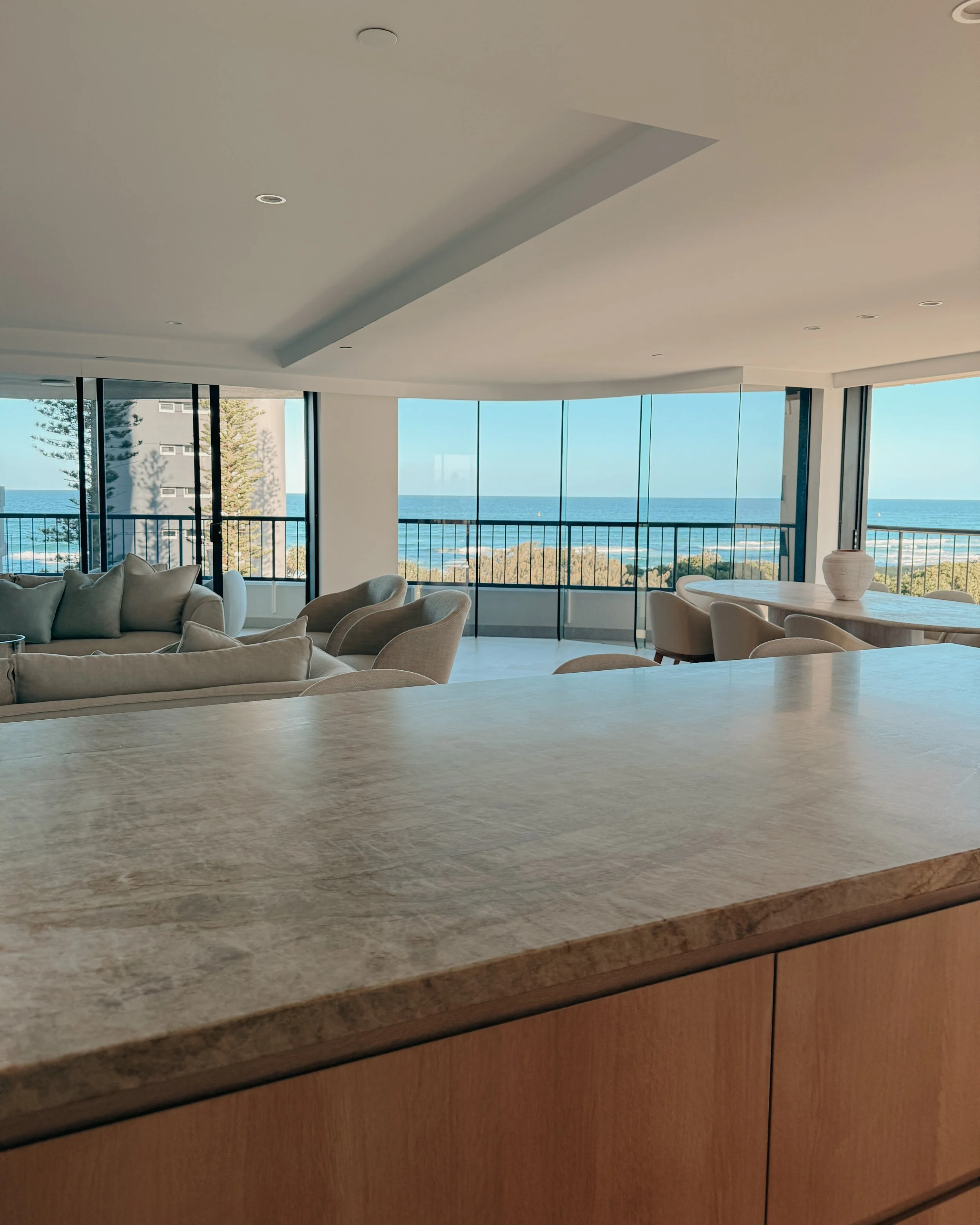 Contemporary condo renovation, modern coastal kitchen with curved island in Taj Mahal stone and pale timber cabinetry in Oceanview Apartment in Gold Coast. Designed by TID Studio Sydney