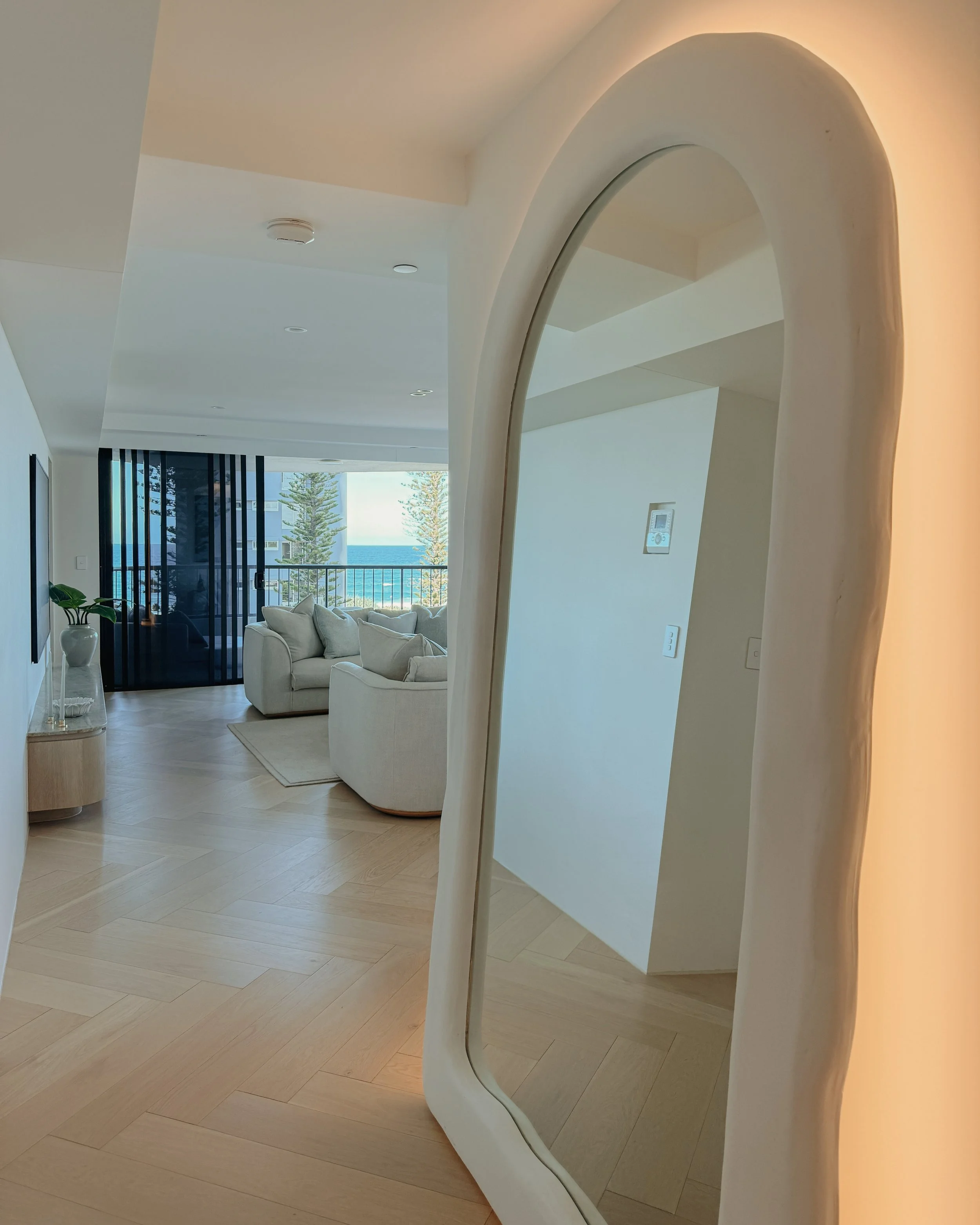 Contemporary condo renovation, modern coastal kitchen with curved island in Taj Mahal stone and pale timber cabinetry, living room seating area in Oceanview Apartment in Gold Coast. Designed by TID Studio Sydney