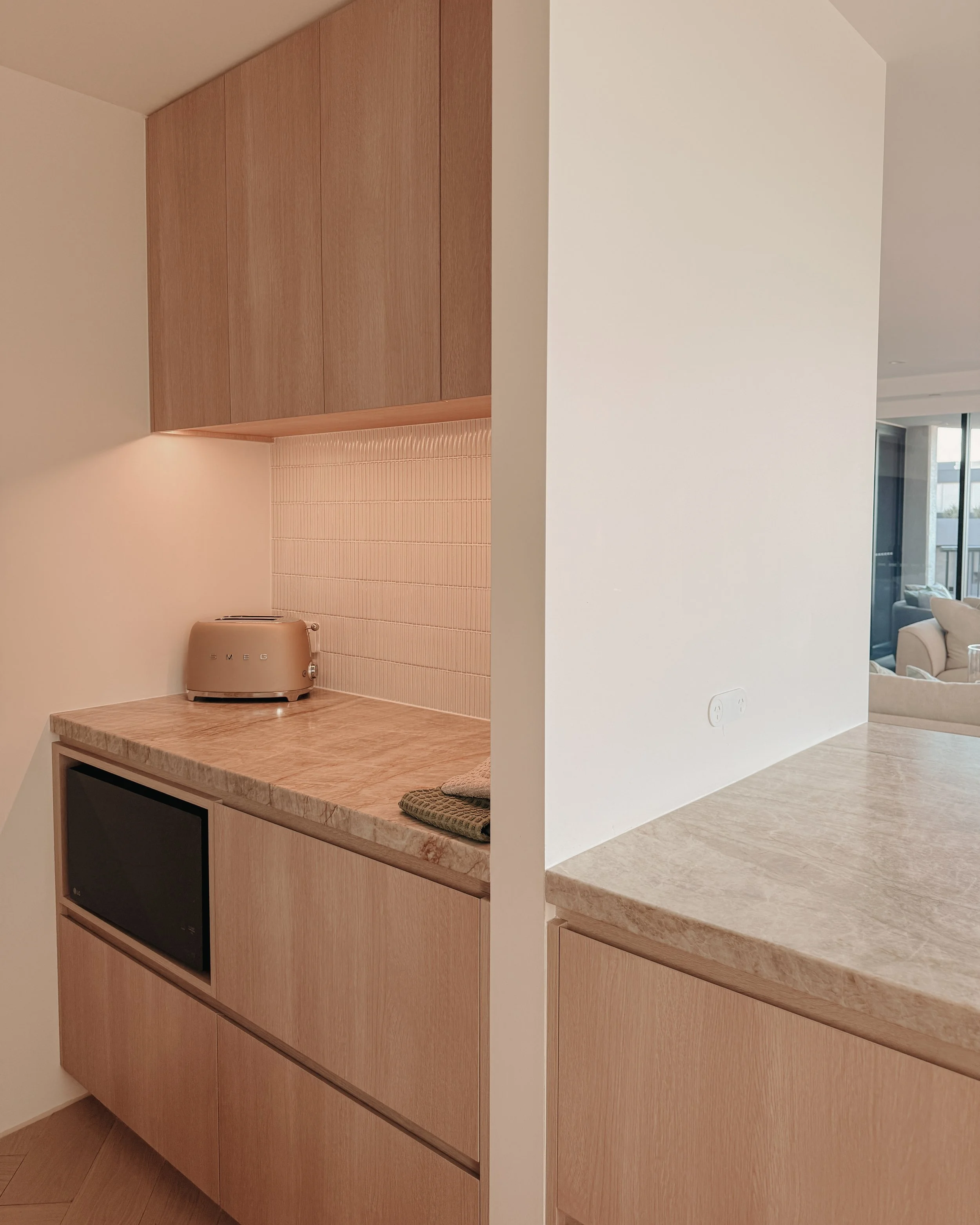 Contemporary condo renovation, modern coastal kitchen with curved island in Taj Mahal stone and pale timber cabinetry in Oceanview Apartment in Gold Coast. Designed by TID Studio Sydney
