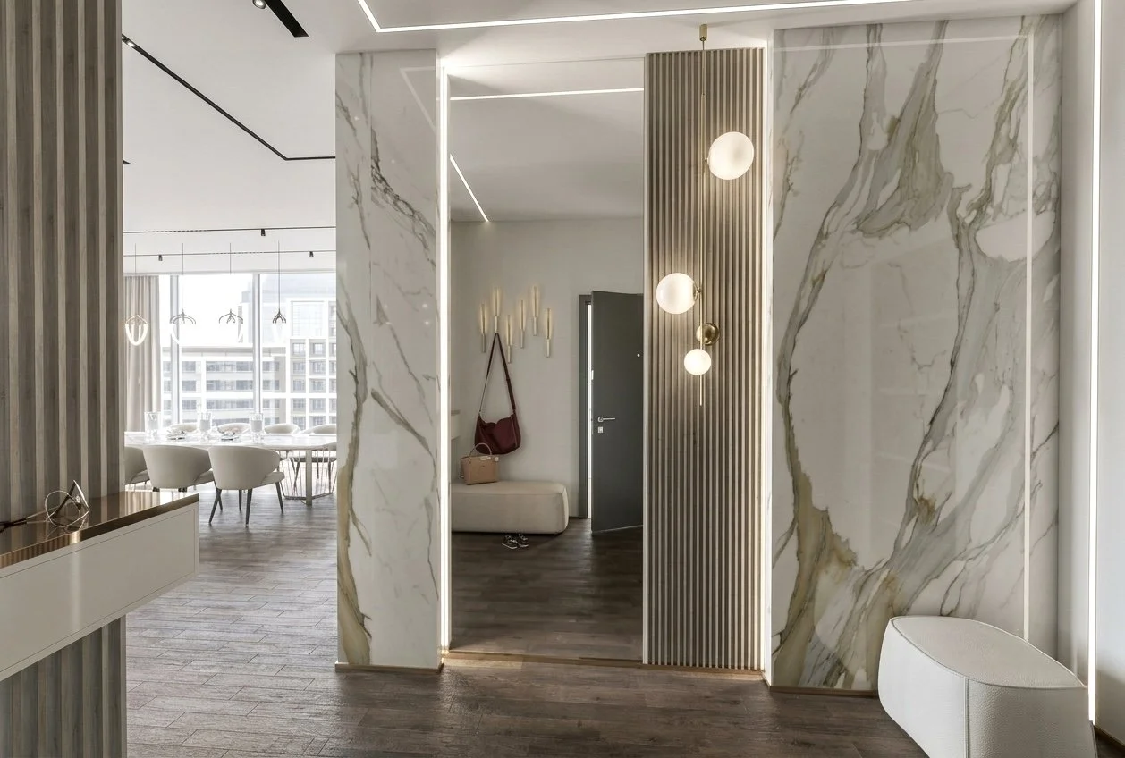 Luxury apartment entryway in Dubai featuring large marble panels, slatted detailing, and warm pendant lighting