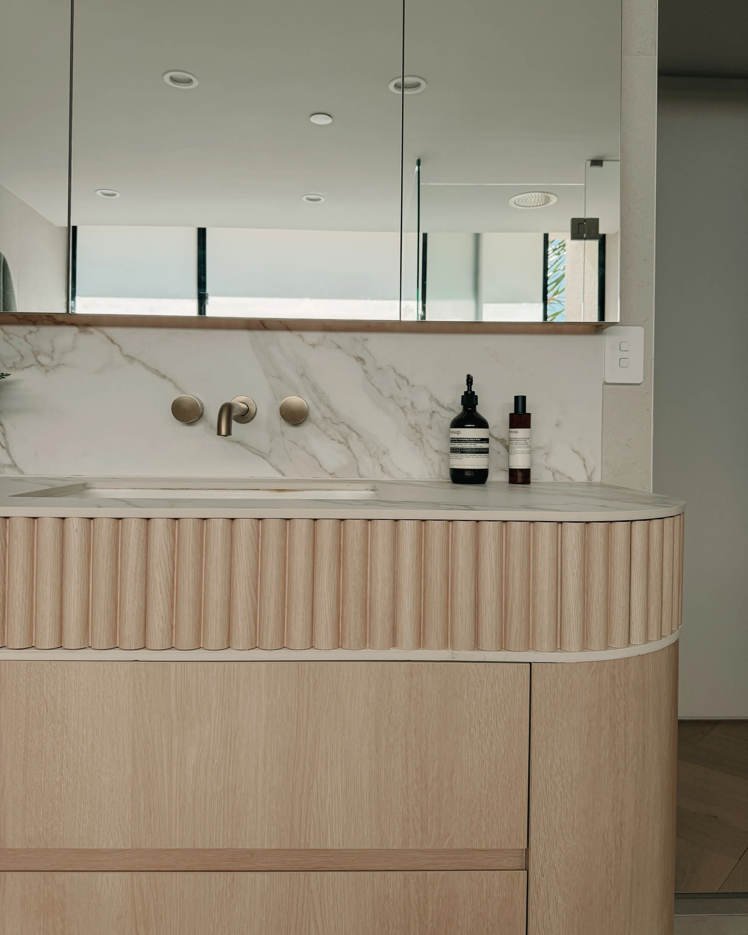 Modern bathroom custom curved vanity, and warm timber tones, fluted timber detail — coastal apartment in Gold Coast designed by TID Studio Sydney