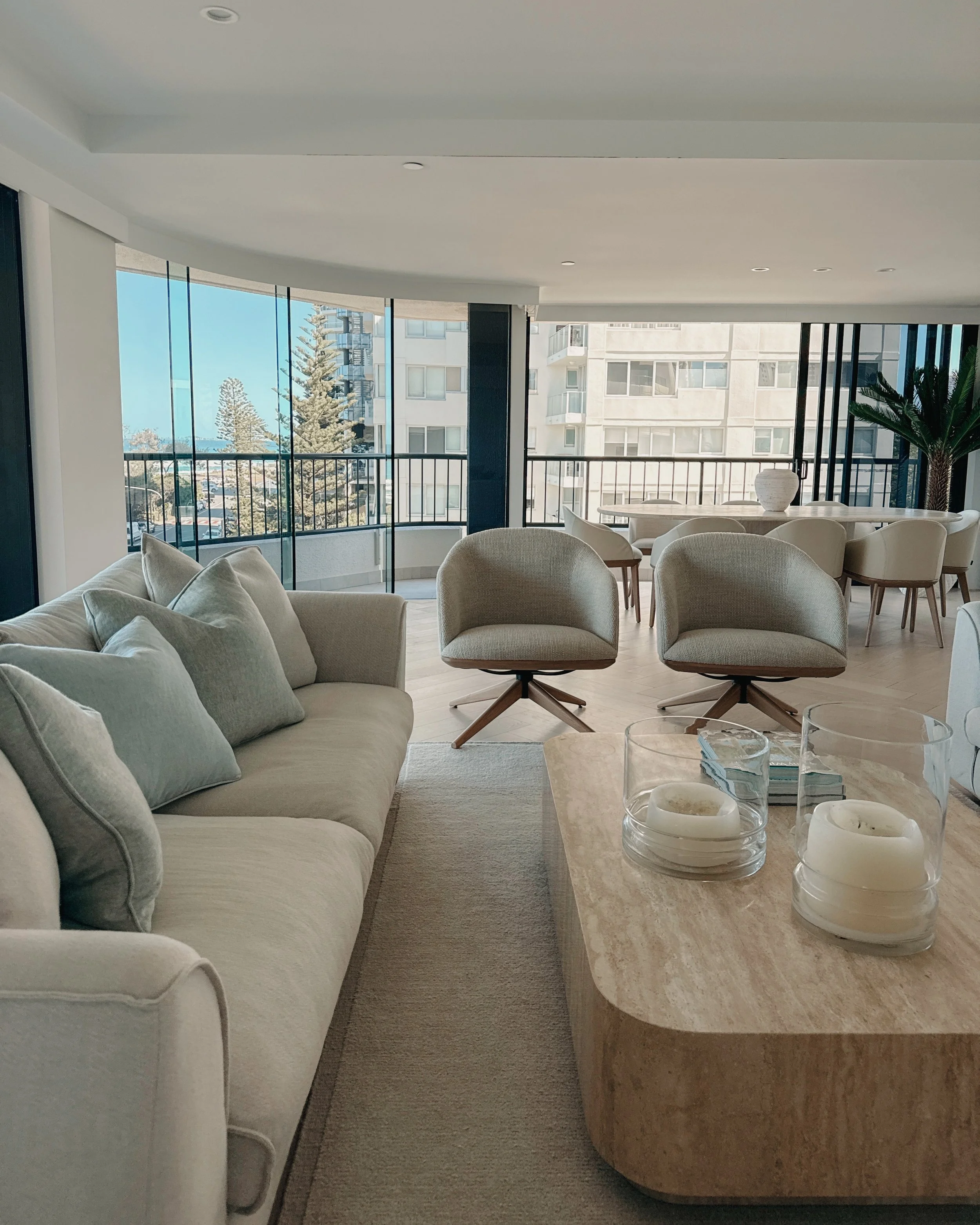 Contemporary condo renovation, modern coastal kitchen with curved island in Taj Mahal stone and pale timber cabinetry, living room seating area in Oceanview Apartment in Gold Coast. Designed by TID Studio Sydney