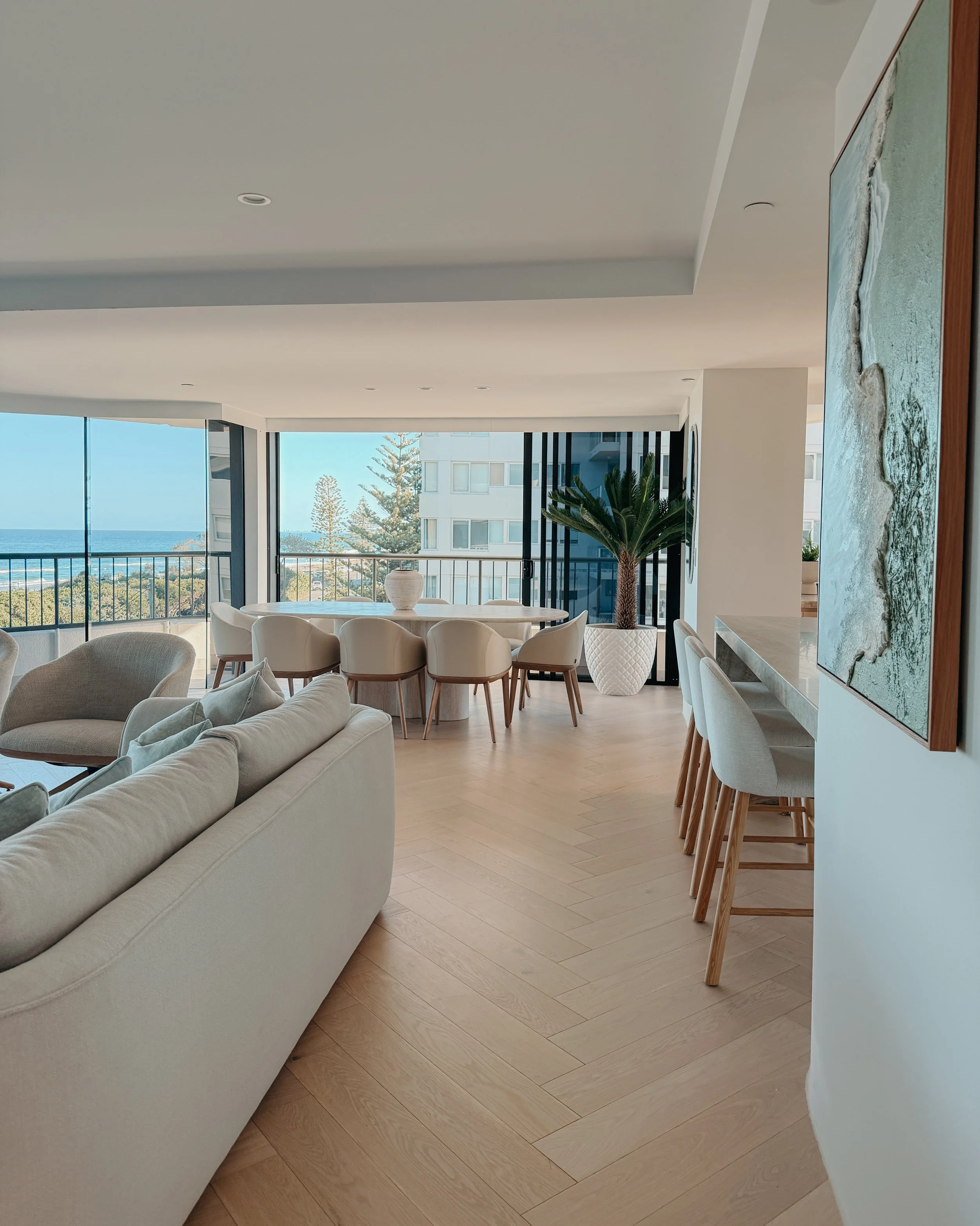 Contemporary condo renovation, modern coastal kitchen with curved island in Taj Mahal stone and pale timber cabinetry, living room seating area in Oceanview Apartment in Gold Coast. Designed by TID Studio Sydney