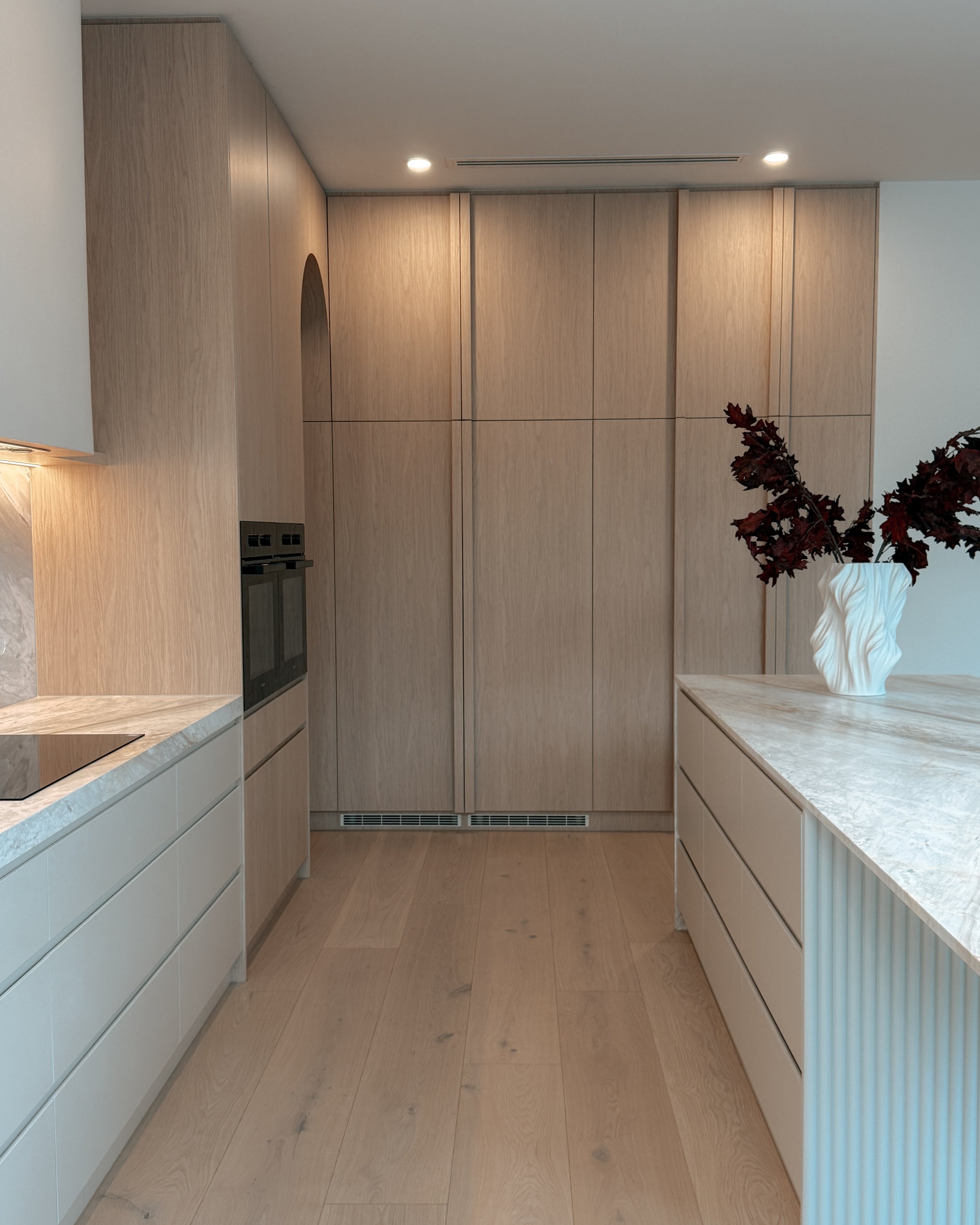 Contemporary soft-curved kitchen with fluted island, light timber cabinetry, and sculptural rangehood in a minimal-luxe Melbourne new-build. Designed by TID Studio, interior design in Sydney