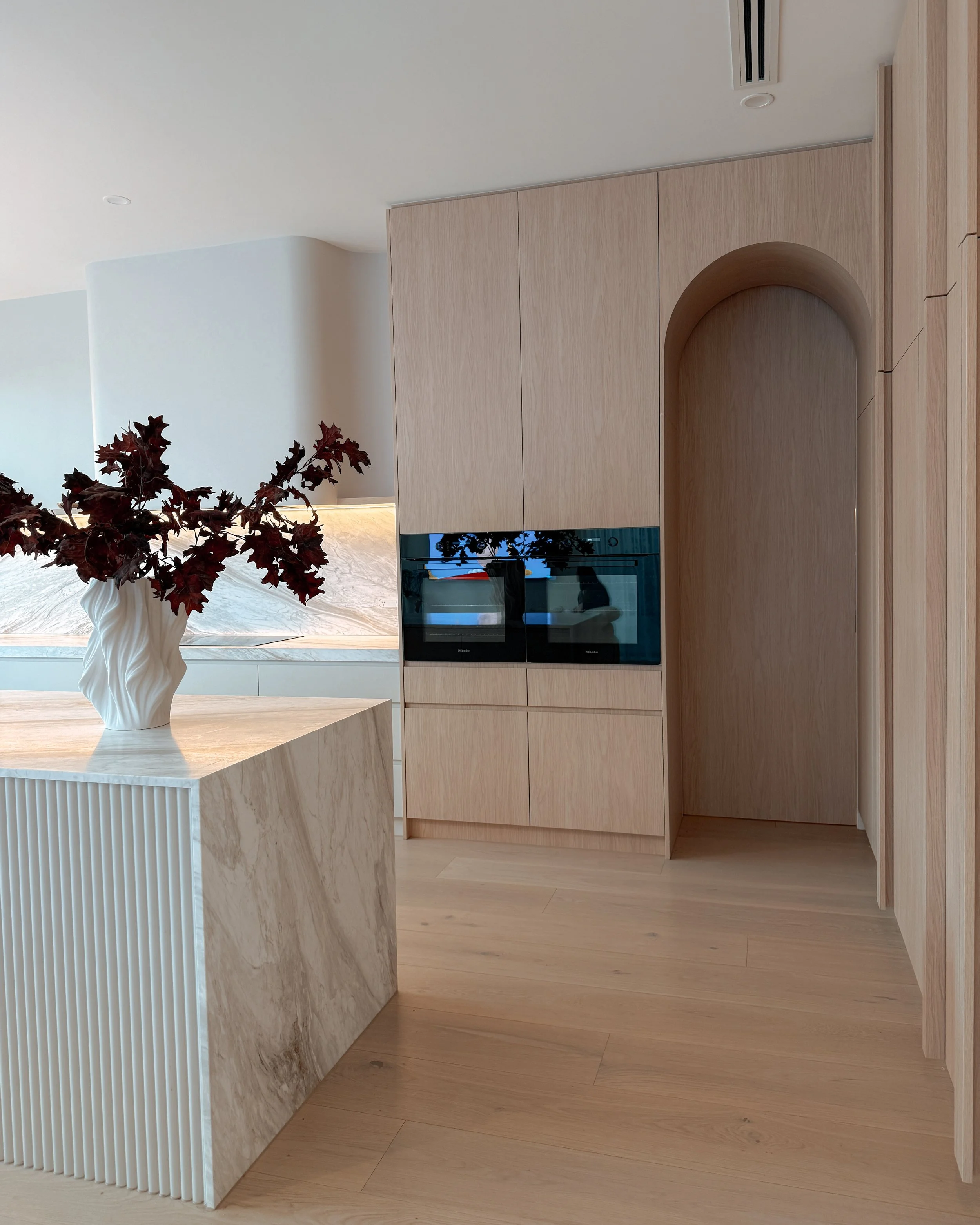 Contemporary soft-curved kitchen with fluted island, light timber cabinetry, and sculptural rangehood in a minimal-luxe Melbourne new-build. Designed by TID Studio, interior design in Sydney