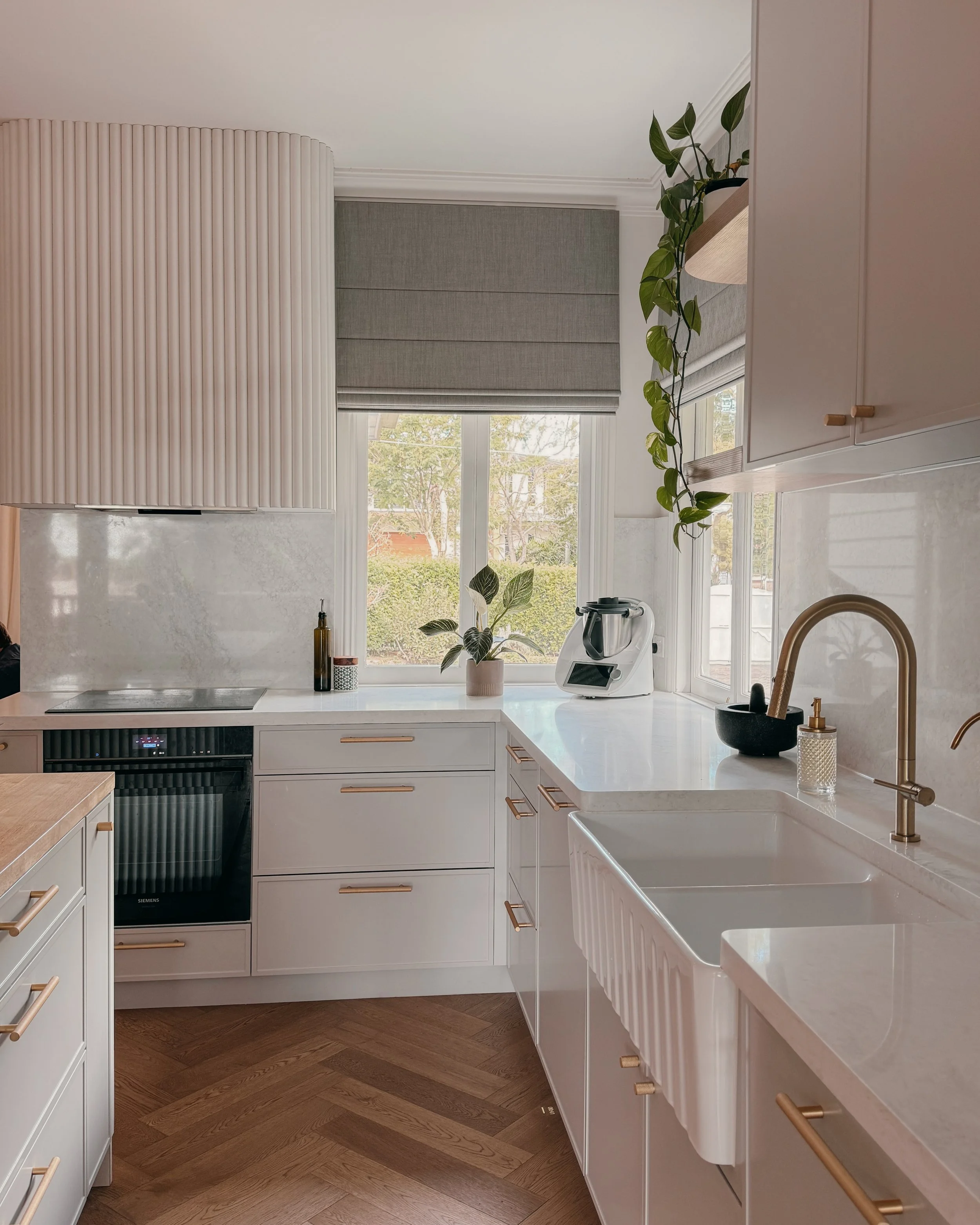 Modern Brisbane kitchen design with curved island, warm timber tones and integrated appliances, soft greige cabinetry, reeded detailing and brass tapware. Interior designer in Sydney