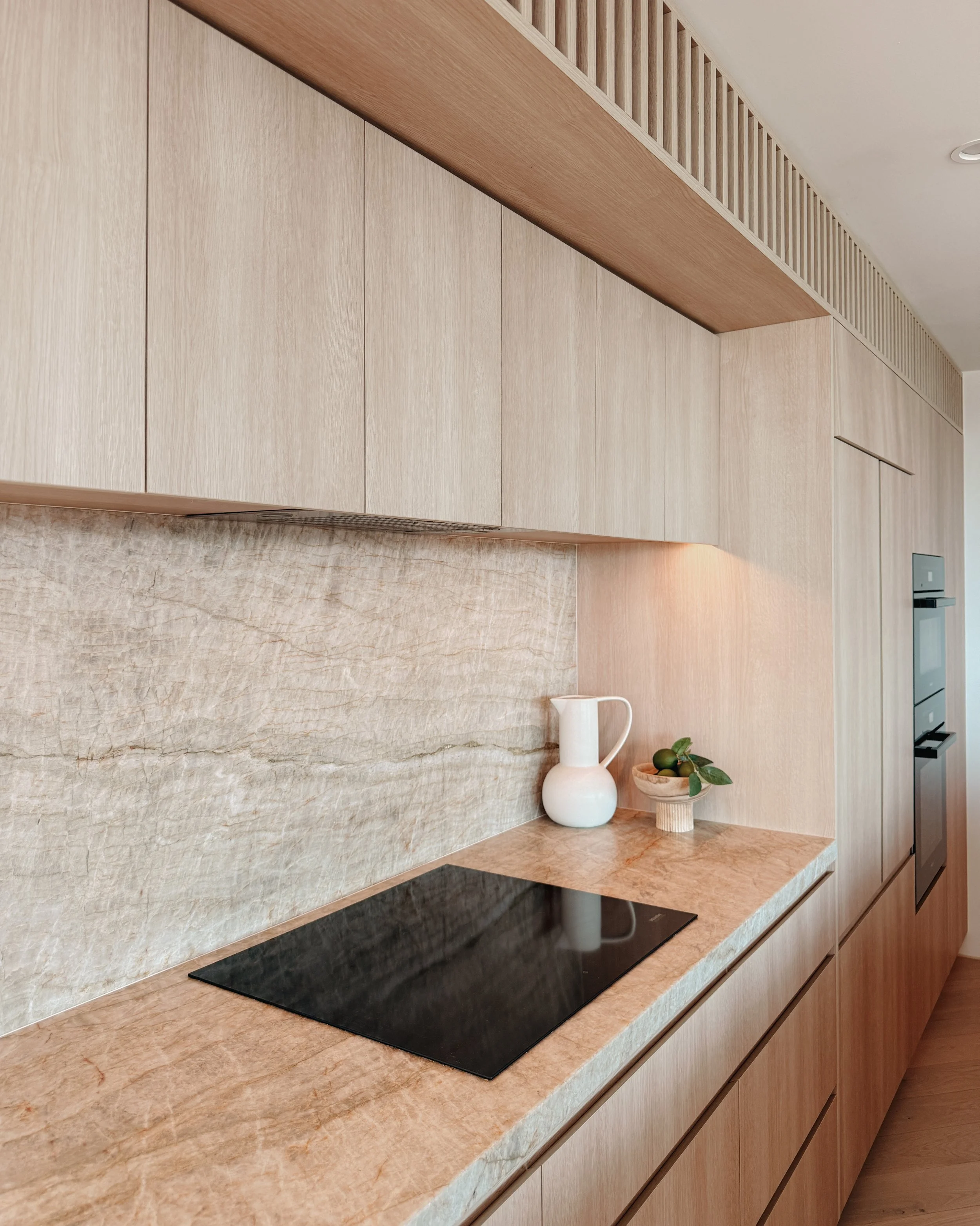 Contemporary condo renovation, modern coastal kitchen with curved island in Taj Mahal stone and pale timber cabinetry in Oceanview Apartment in Gold Coast. Designed by TID Studio Sydney