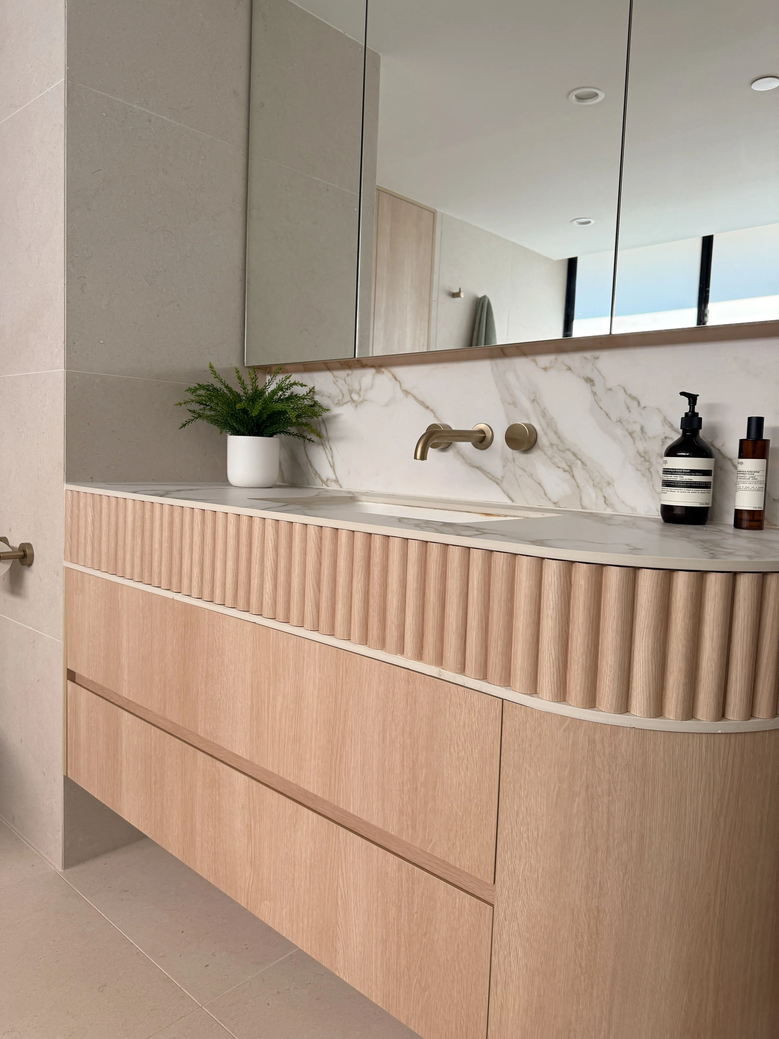 Modern bathroom custom curved vanity, and warm timber tones, fluted timber detail — coastal apartment in Gold Coast designed by TID Studio Sydney