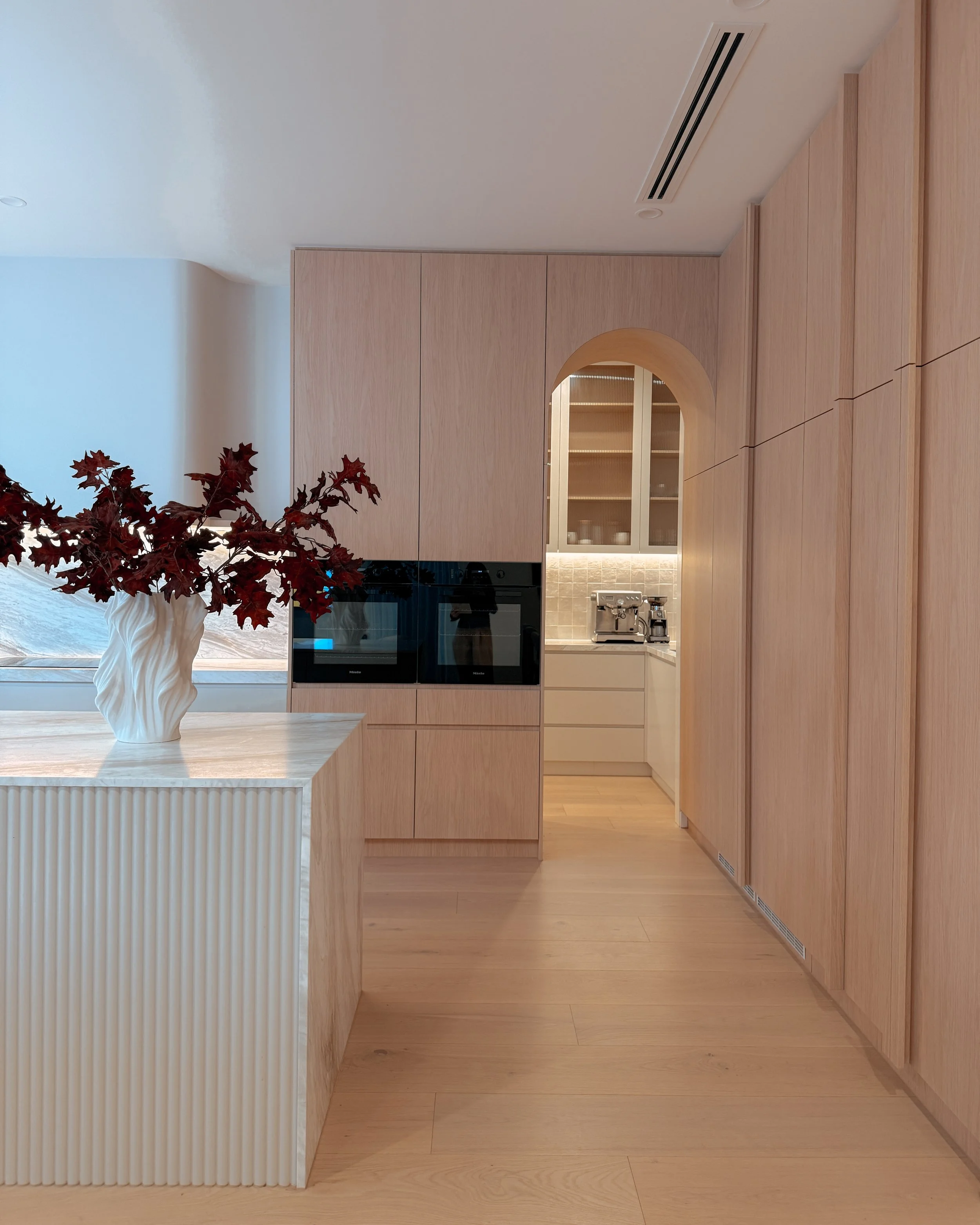 Contemporary soft-curved kitchen with fluted island, light timber cabinetry, and sculptural rangehood in a minimal-luxe Melbourne new-build. Designed by TID Studio, interior design in Sydney