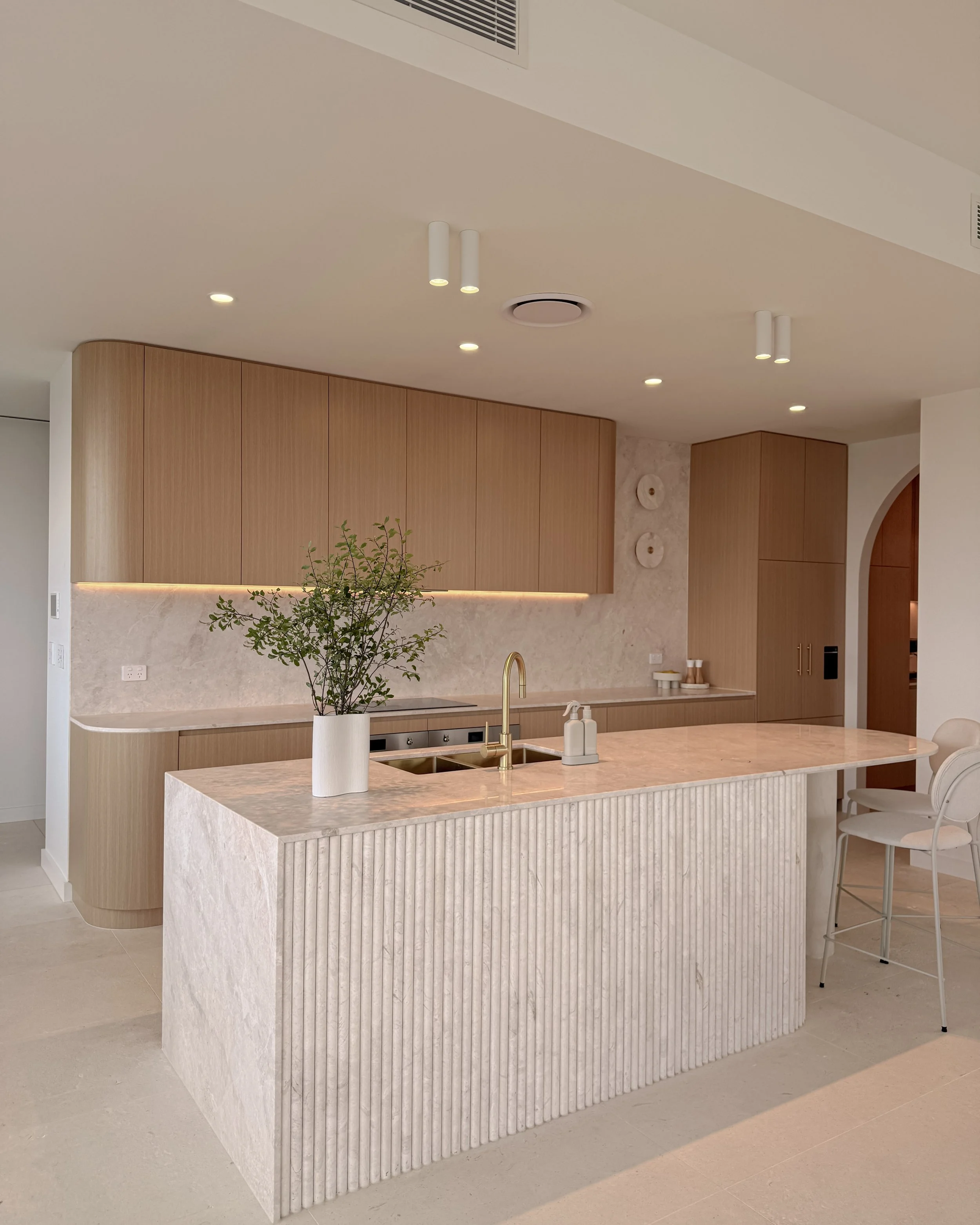 Modern coastal kitchen and pantry designed by TID Studio. Contemporary kitchen with curved cabinetry and fluted stone kitchen island. Sydney interior designer