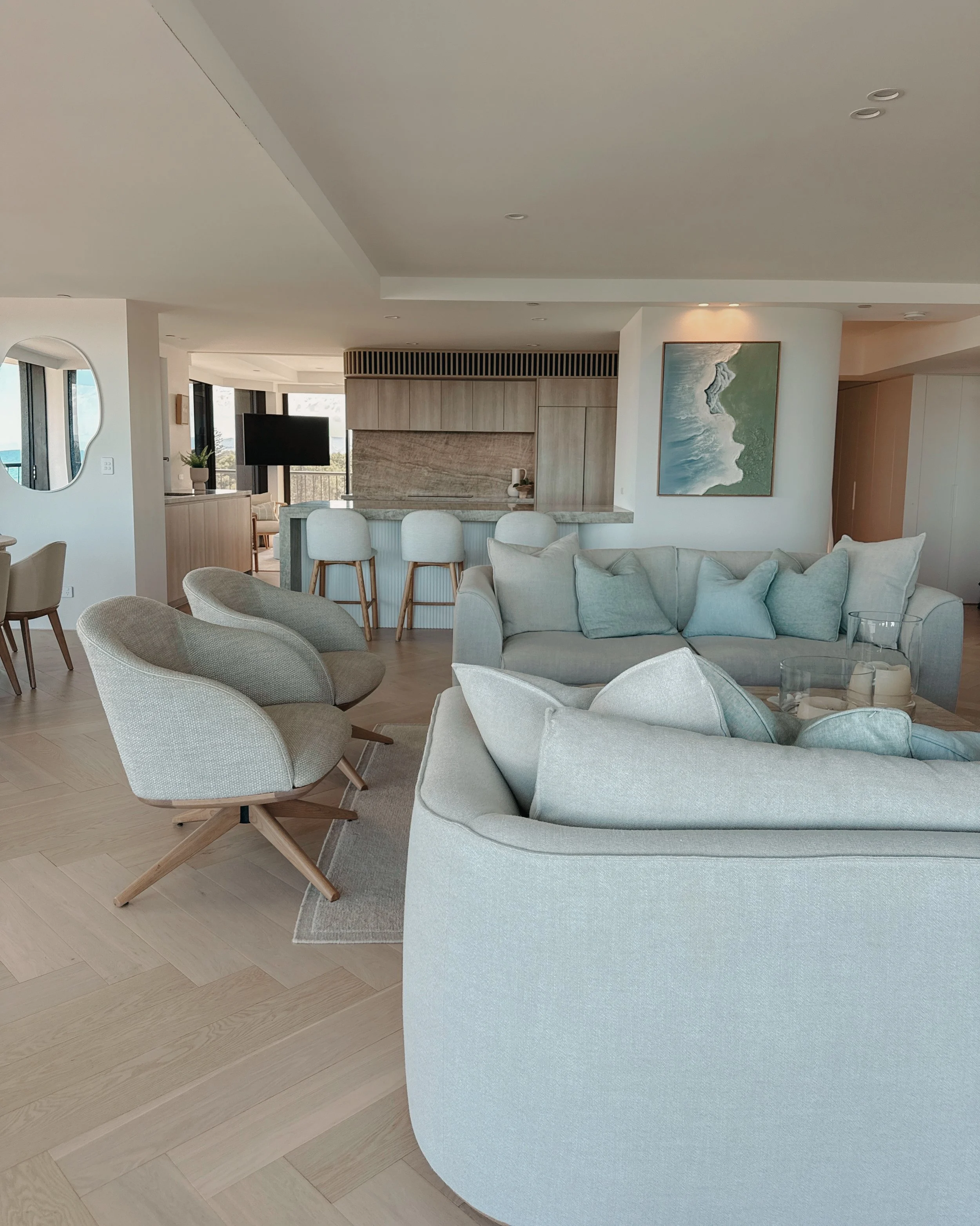 Contemporary condo renovation, modern coastal kitchen with curved island in Taj Mahal stone and pale timber cabinetry, living room seating area in Oceanview Apartment in Gold Coast. Designed by TID Studio Sydney