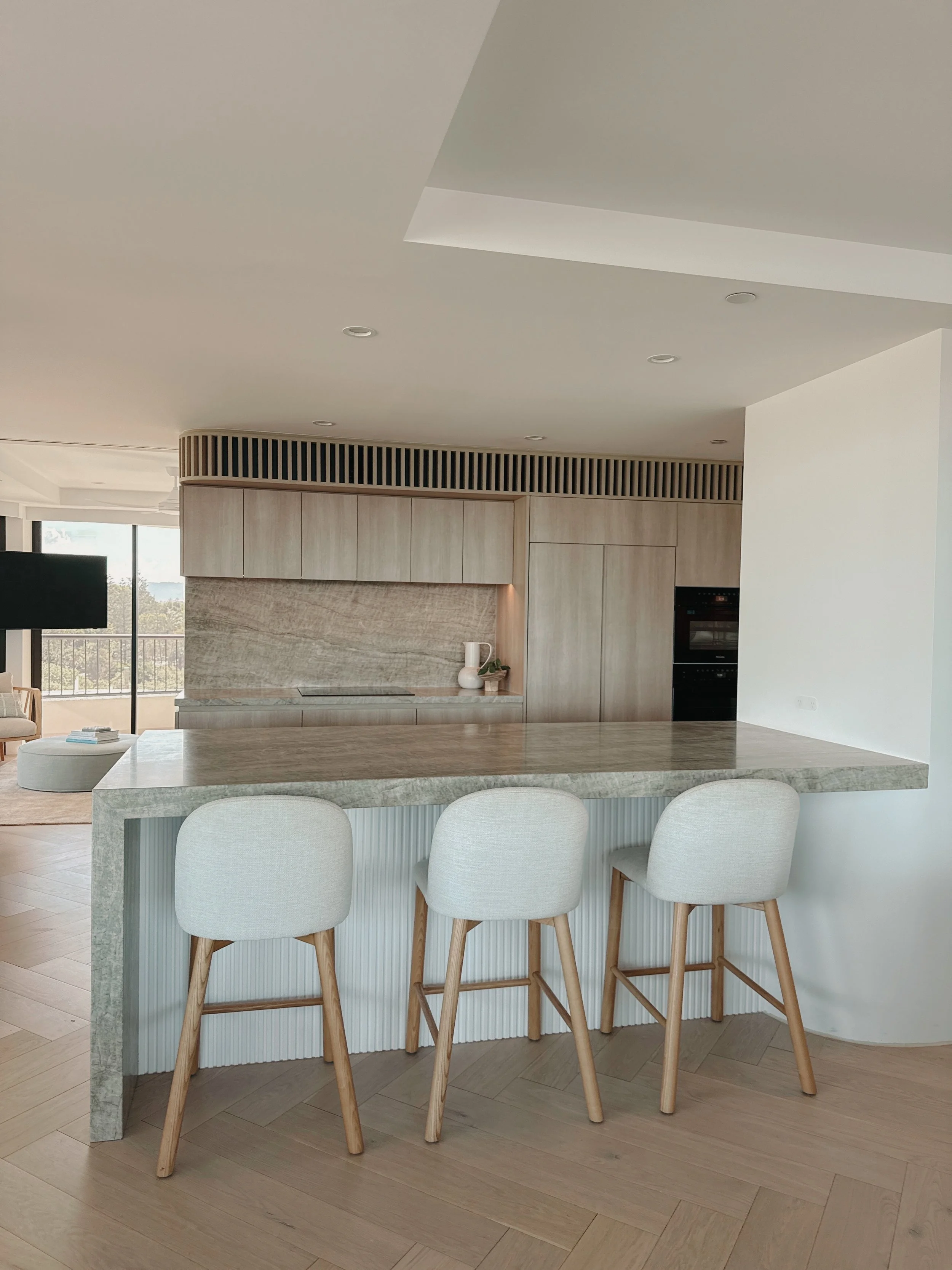 Contemporary coastal kitchen with curved island and pale timber cabinetry in Oceanview Apartment Gold Coast