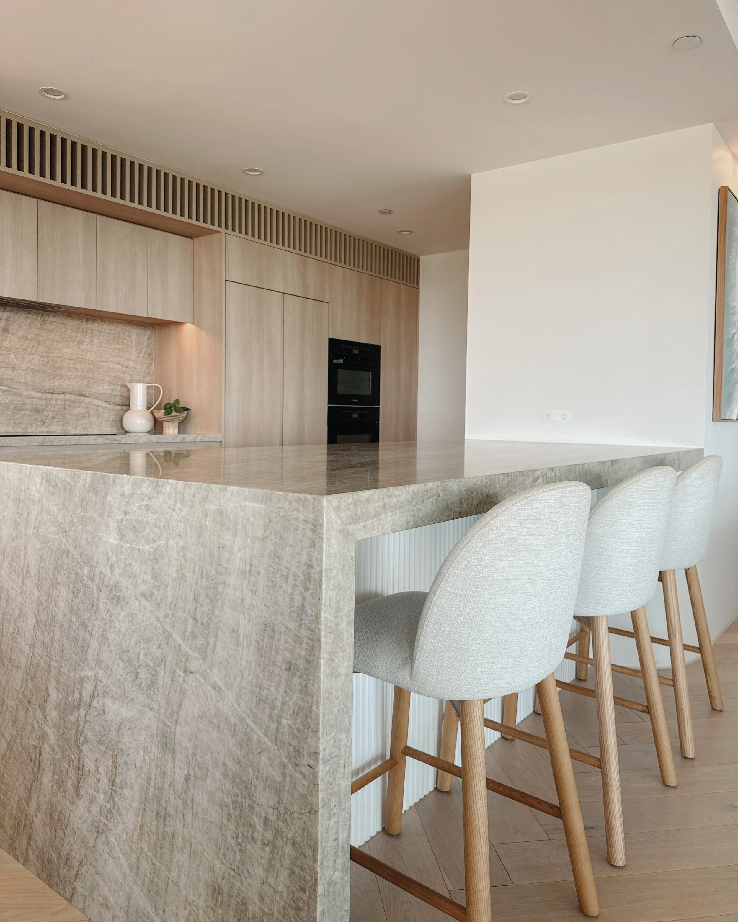 Contemporary condo renovation, modern coastal kitchen with curved island in Taj Mahal stone and pale timber cabinetry in Oceanview Apartment in Gold Coast. Designed by TID Studio Sydney