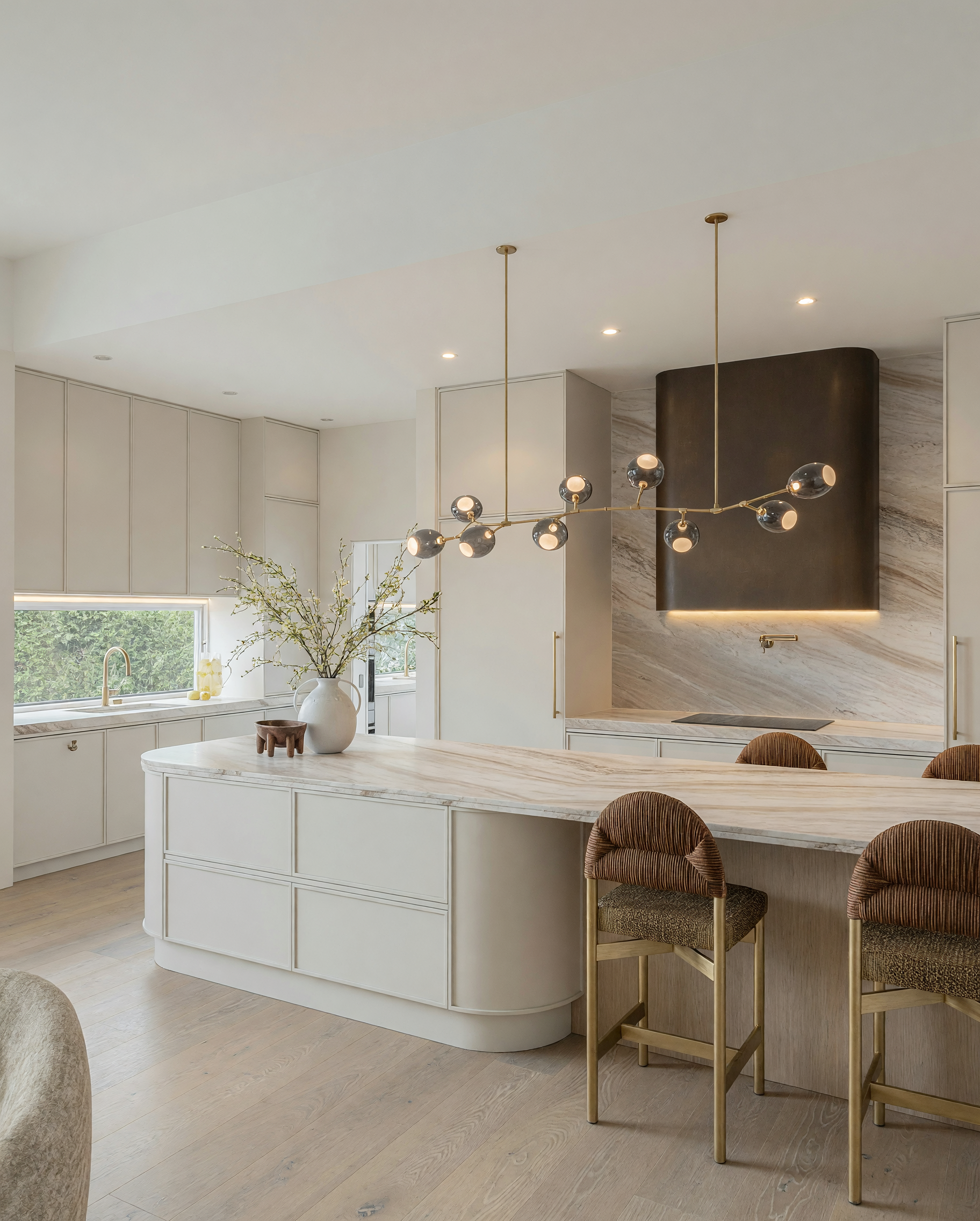 Modern luxury kitchen featuring Taj Mahal stone curved island, warm oak cabinetry, bronze rangehood and custom pantry design