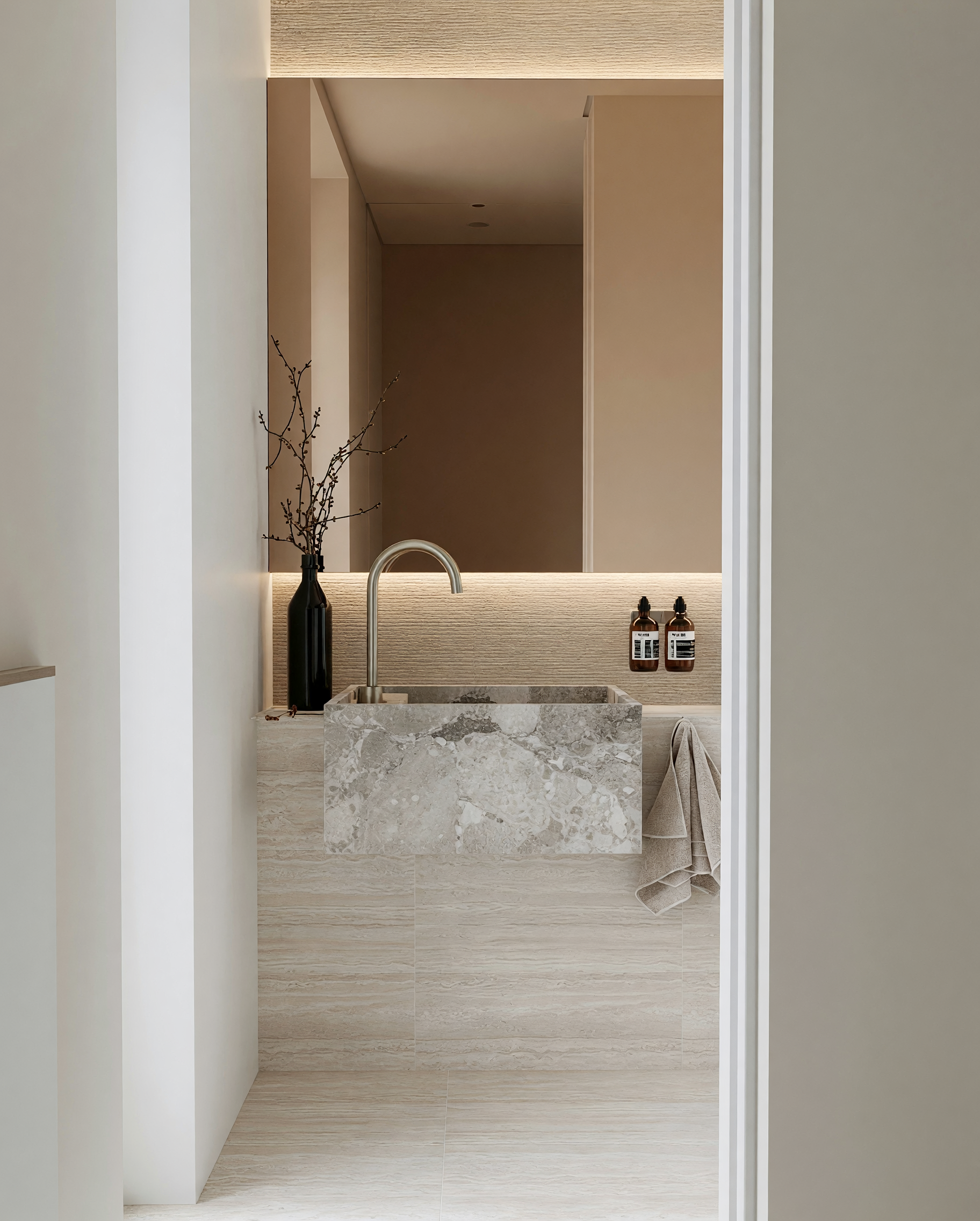 Luxury powder room with stone sink, creamy tiles, bronze fixtures and contemporary lighting